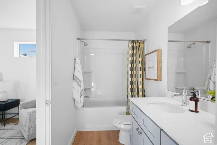 Bright and spa-like primary bathroom featuring a double-sink vanity with white cabinetry and quartz countertop, frameless glass shower enclosure with subway tile surround, wood-finish flooring, and brushed nickel fixtures throughout
