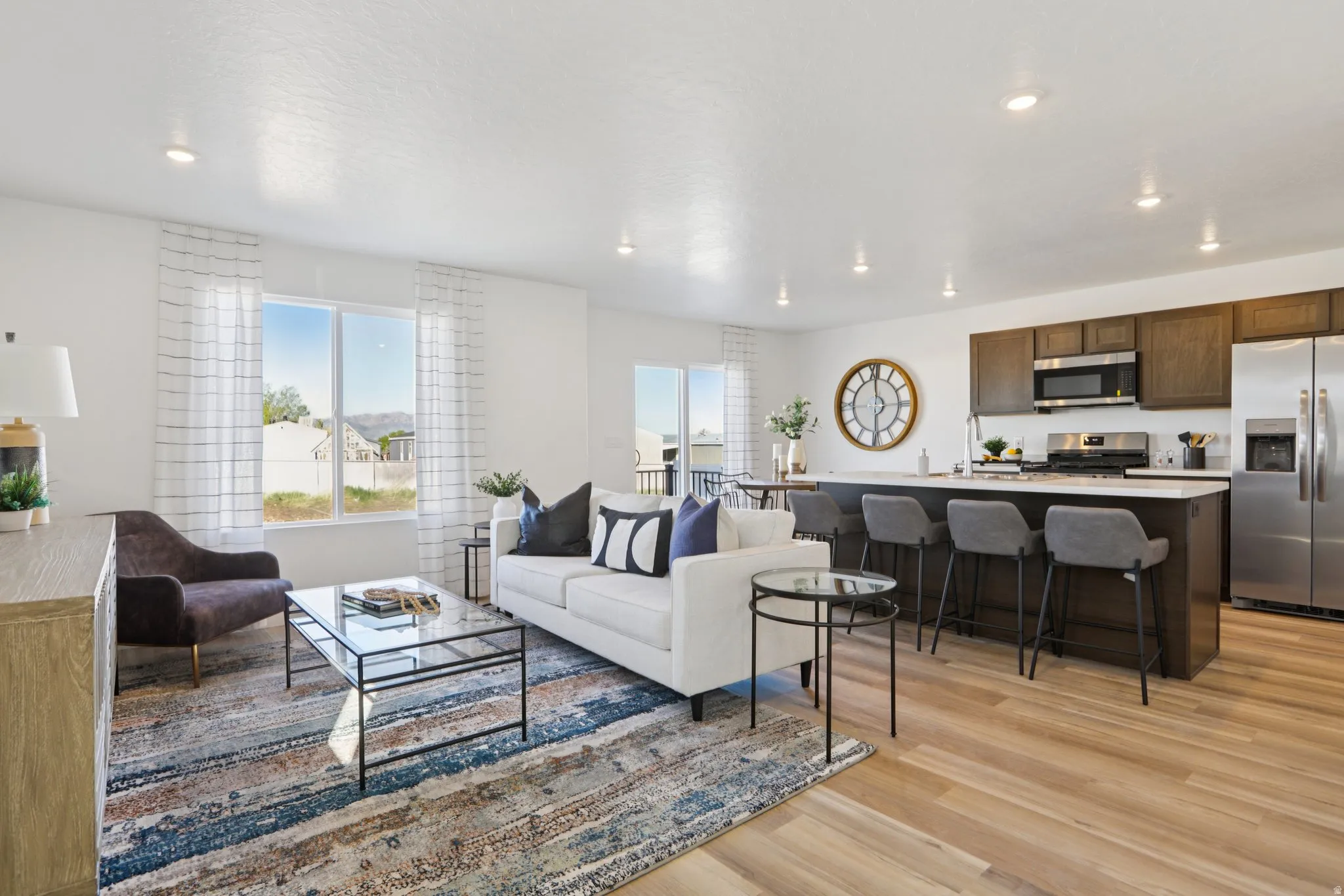 Open-concept living area with wood-finish flooring, recessed lighting, and a kitchen featuring dark wood cabinetry, stainless steel appliances, and an island with bar seating