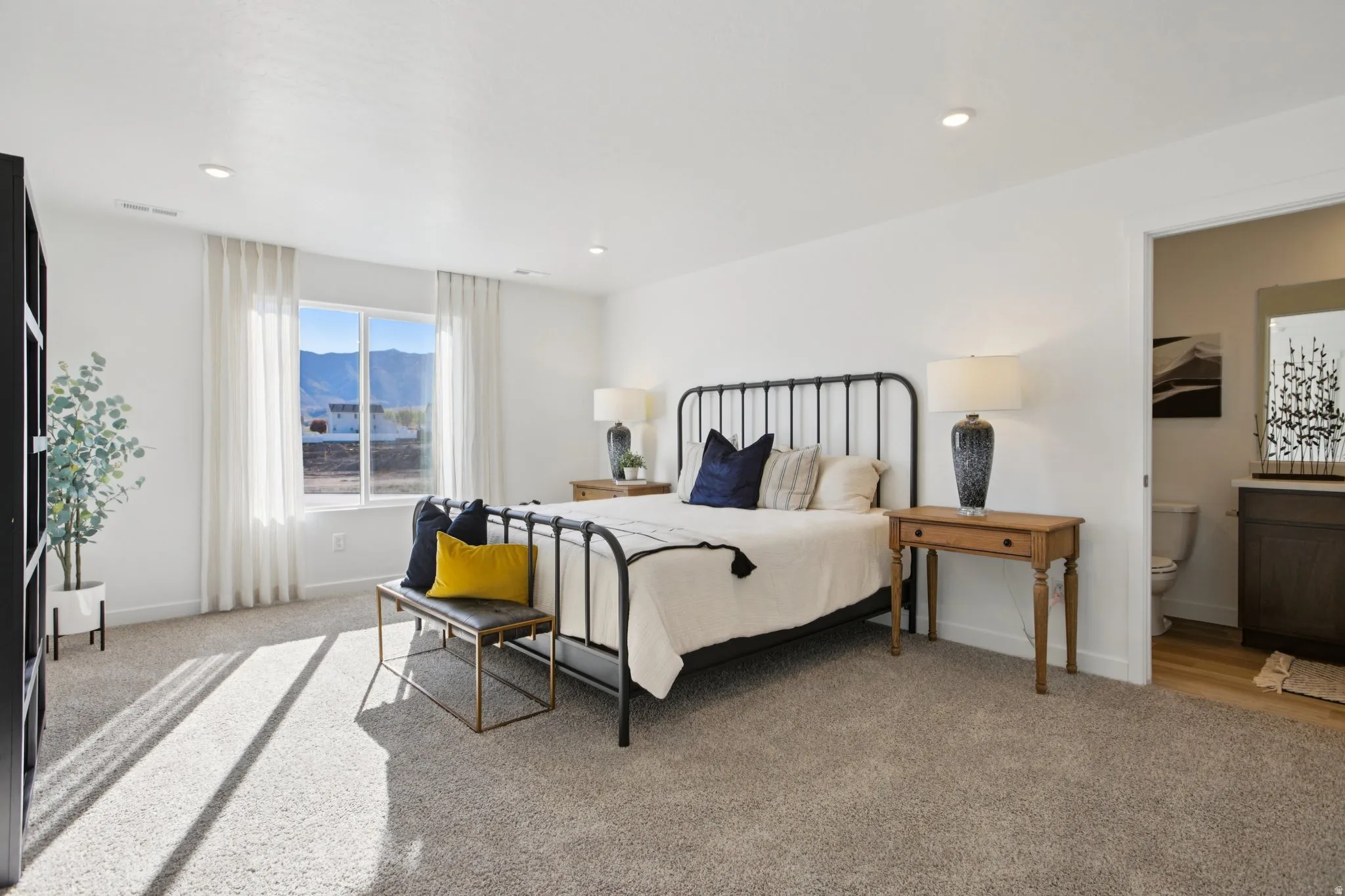 Wall-to-wall carpeting with recessed lighting, a large window, and an en-suite bathroom with a vanity and wood-finish flooring