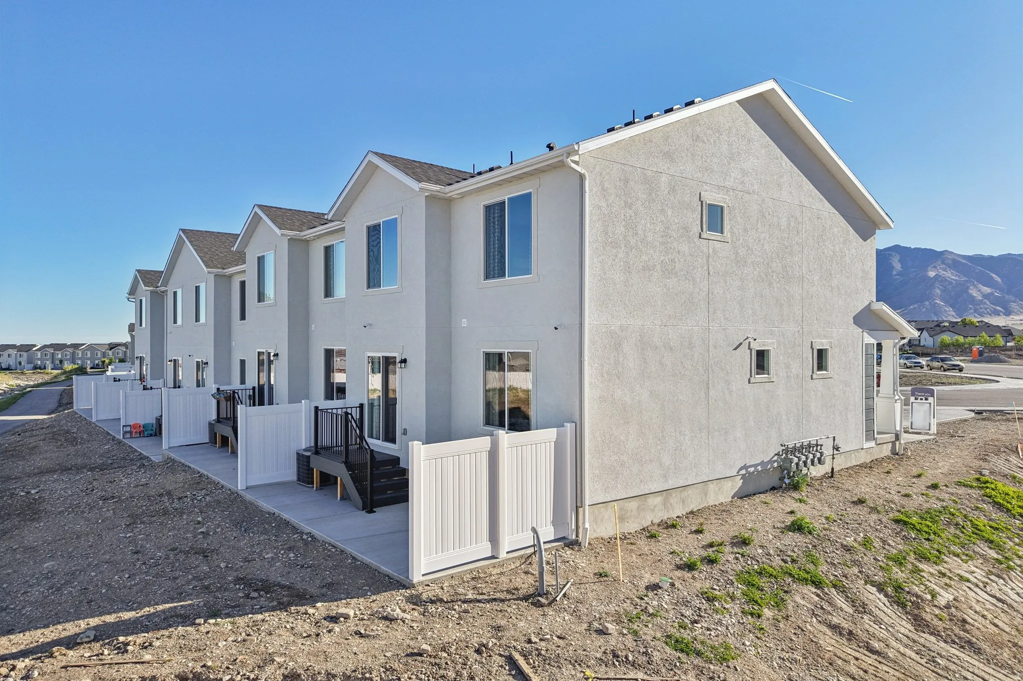 Stucco exterior with multiple windows, individual patio spaces, white privacy fencing, and dark-stained decks