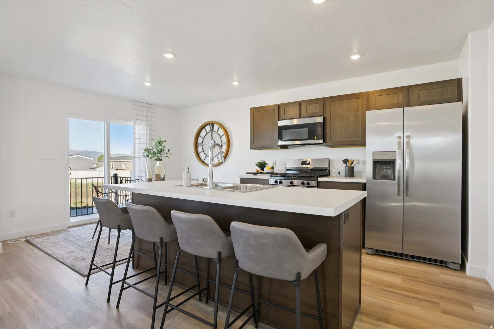 Modern kitchen featuring a large central island, stainless steel appliances, dark wood-finish cabinetry, light countertops, and wood-finish flooring