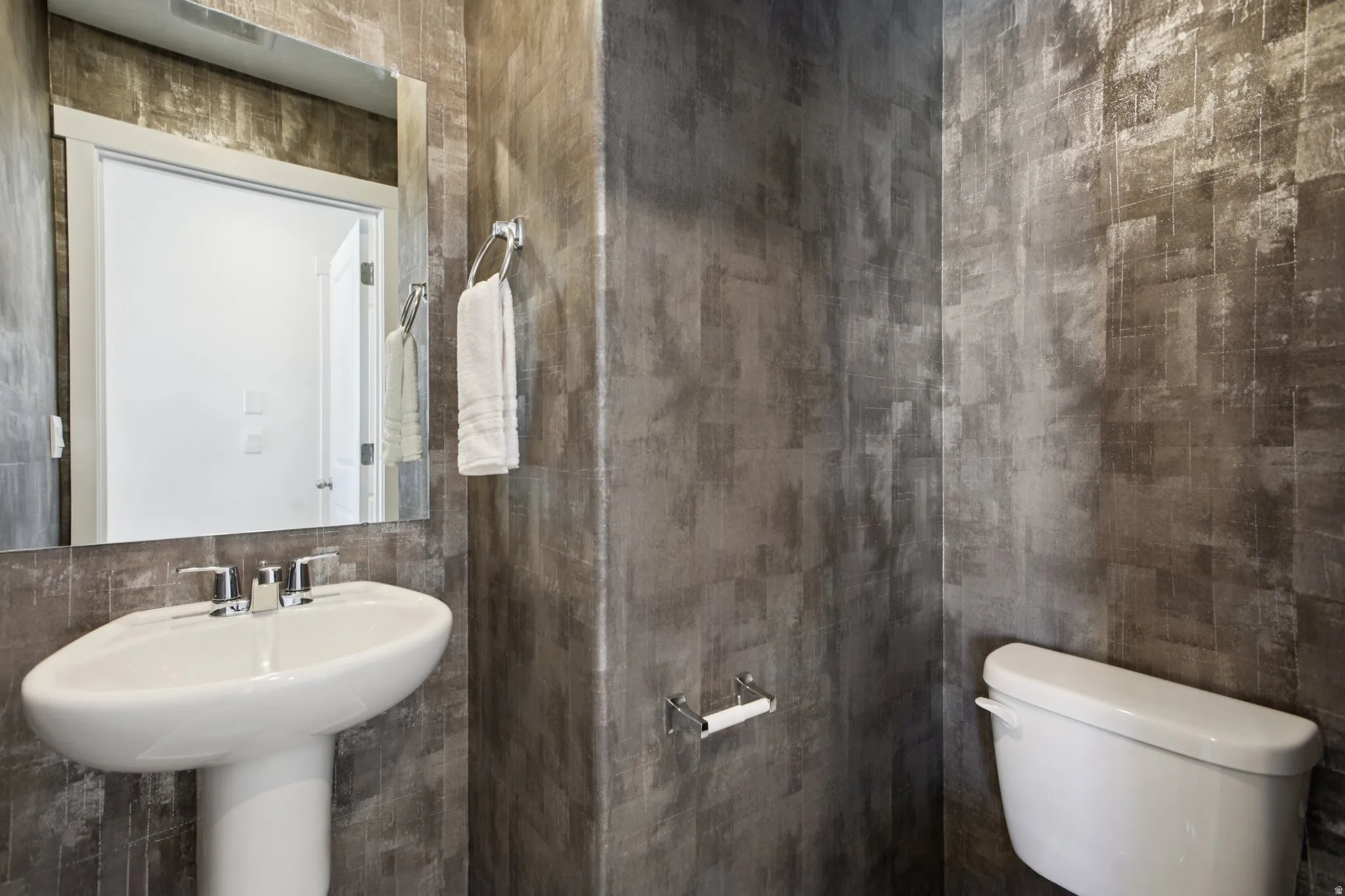 Pedestal sink with chrome fixtures, wall-mounted mirror, and textured wall finish