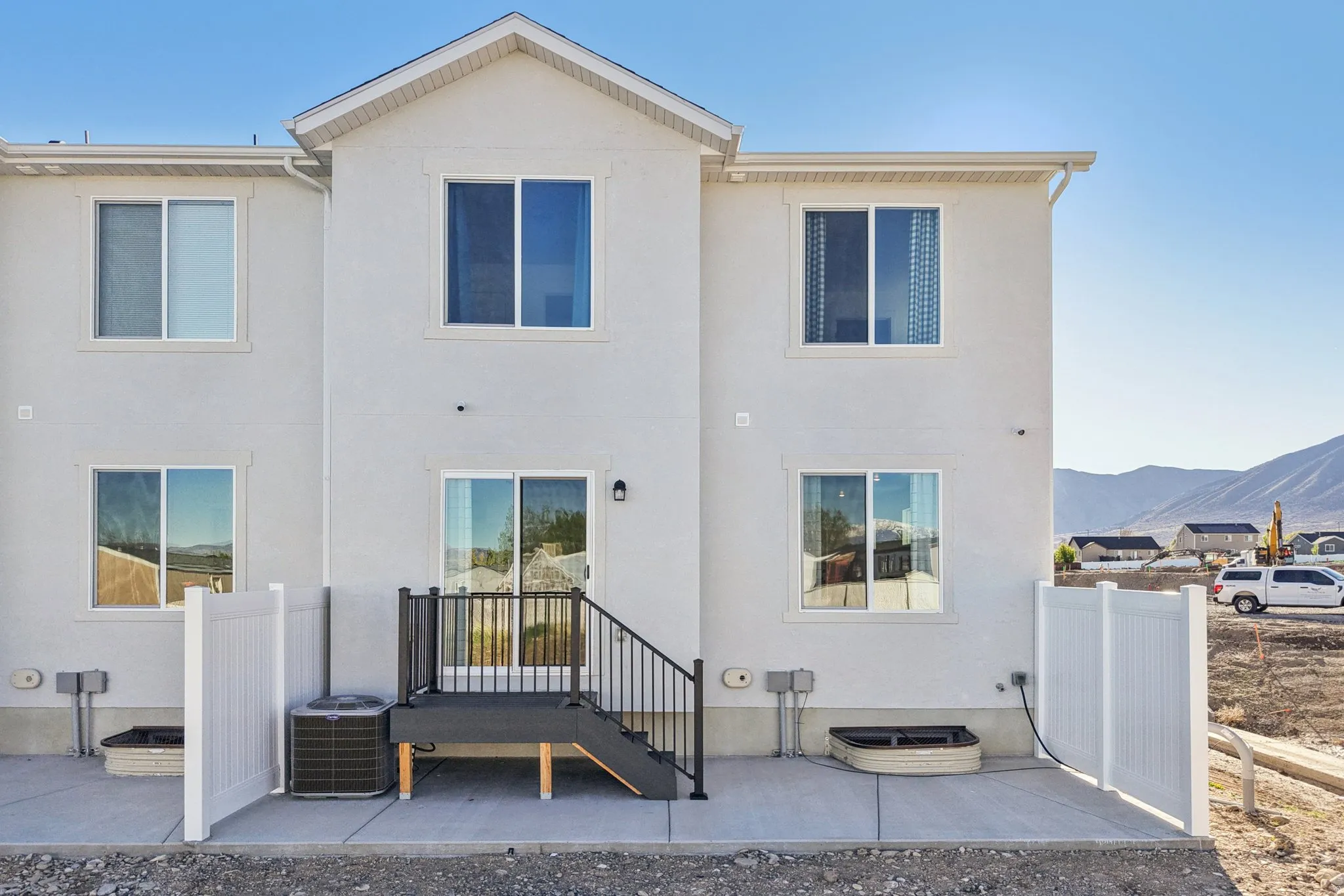 Rear exterior with a concrete patio, white privacy fencing, and a two-story design featuring multiple windows and a sliding glass door
