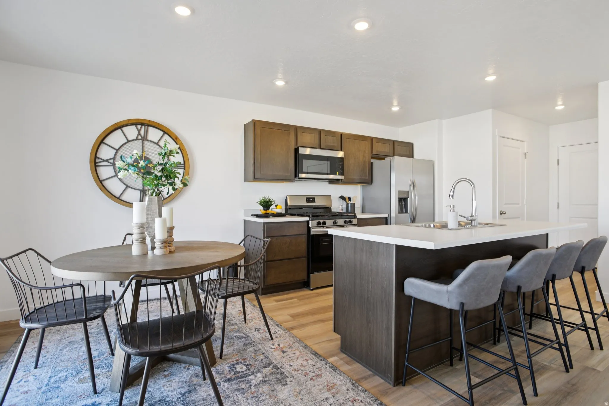 Kitchen with wood-finish flooring, dark wood-finish cabinetry, stainless steel appliances, and a kitchen island with seating