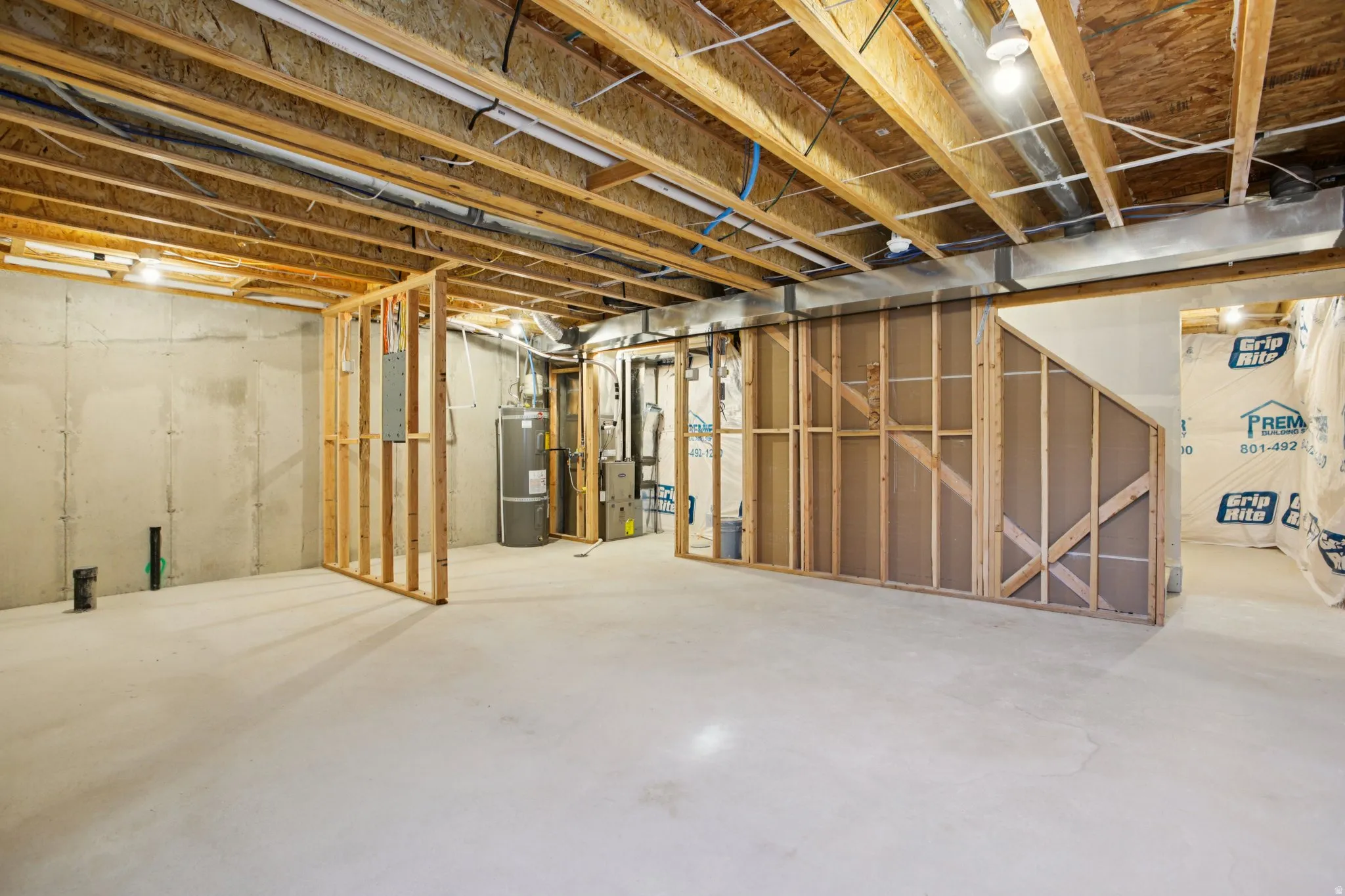 Unfinished basement with concrete flooring, exposed wood joists, framed wall sections, and visible utility systems