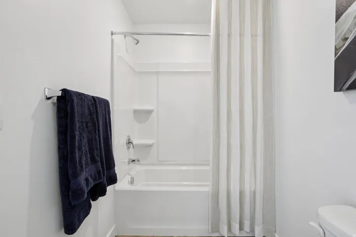 Bathtub with integrated shower, chrome fixtures, and a bright white surround