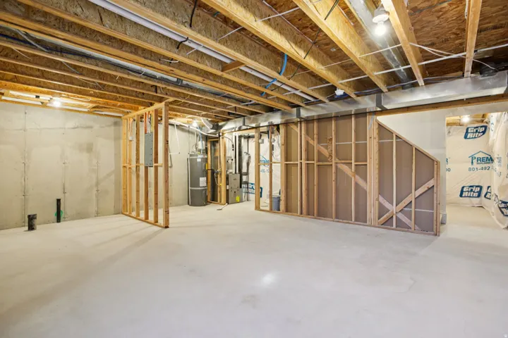 Unfinished basement with concrete flooring, exposed wood joists, framed wall sections, and visible utility systems