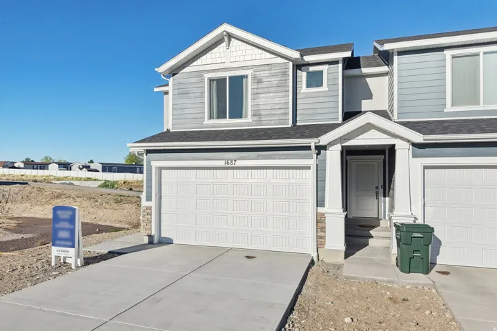 Two-story exterior with light blue horizontal siding, white trim, stone accents, two attached garages, and a covered entry