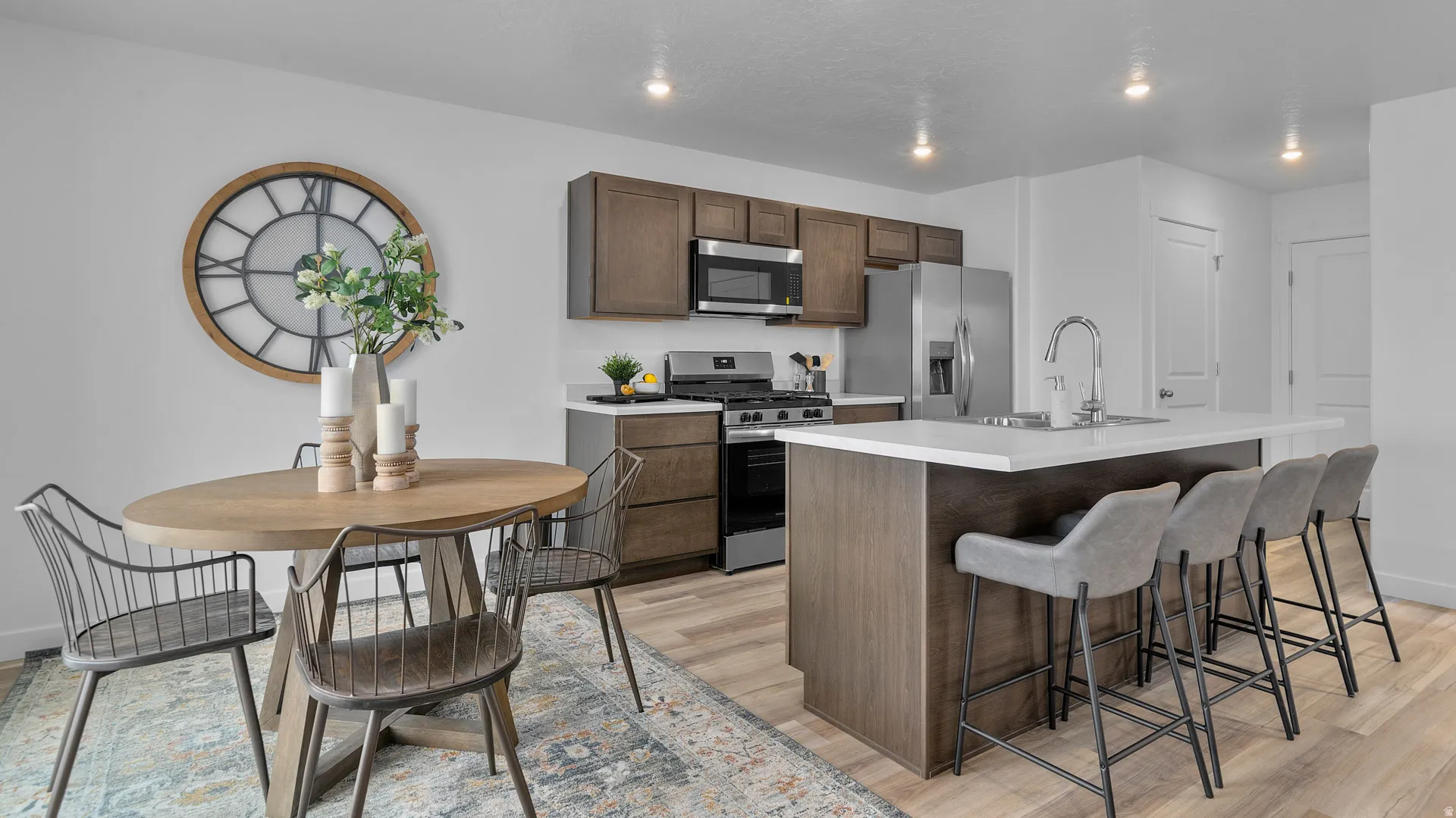 Kitchen featuring wood-finish flooring, dark wood-finish cabinetry, stainless steel appliances, a center island with sink, and solid surface countertops