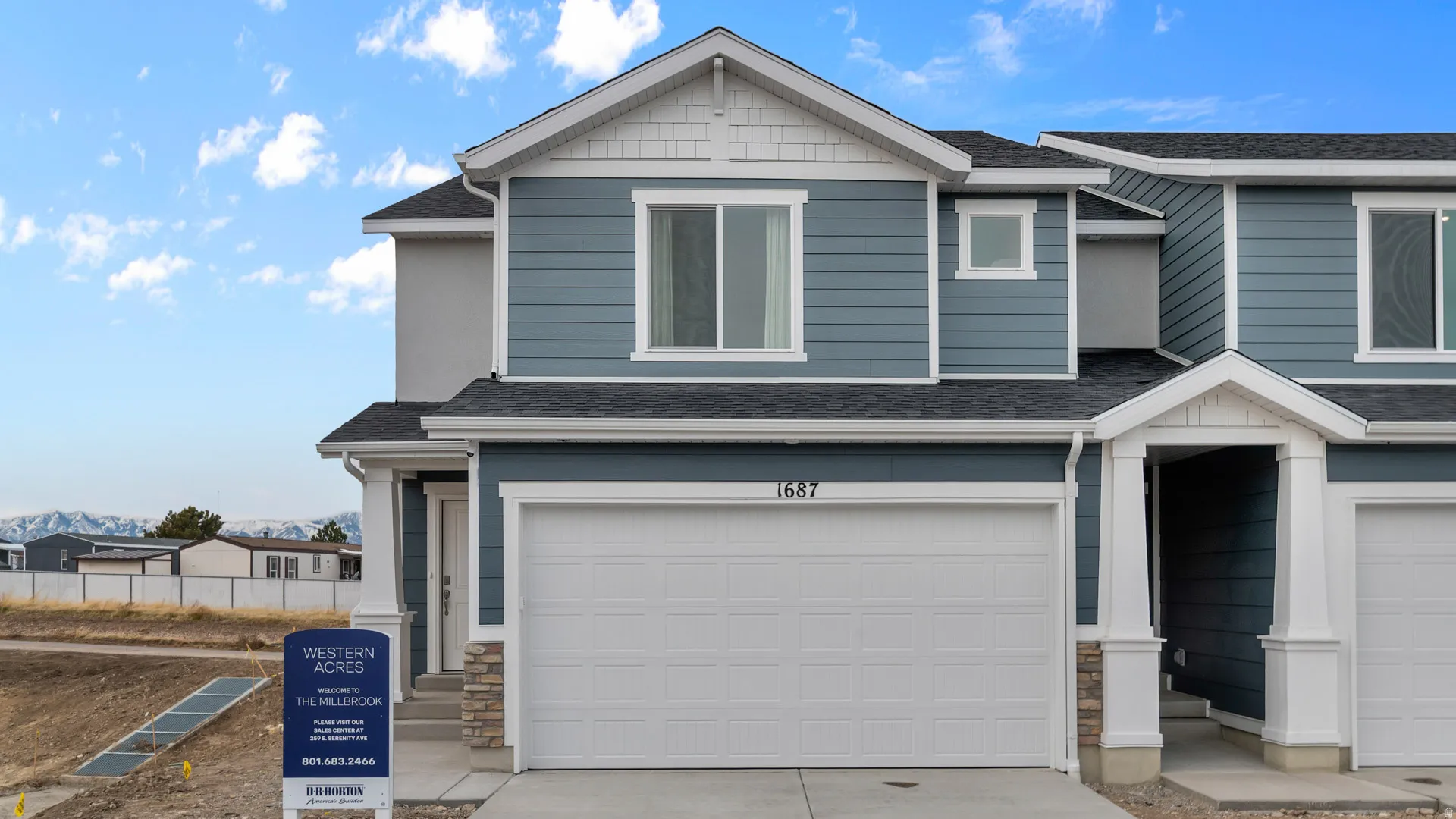 Blue siding exterior with white trim, stone accents, two-car garage, and covered entryway