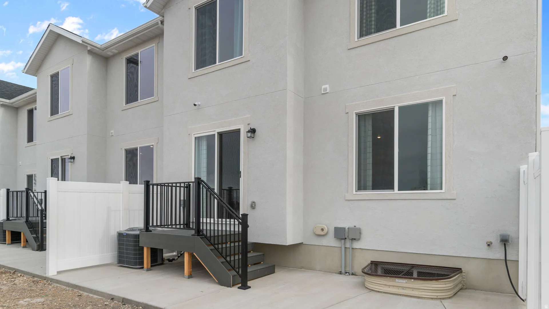 Concrete patio area with privacy fencing, dark gray deck with black railings, and sliding glass door access