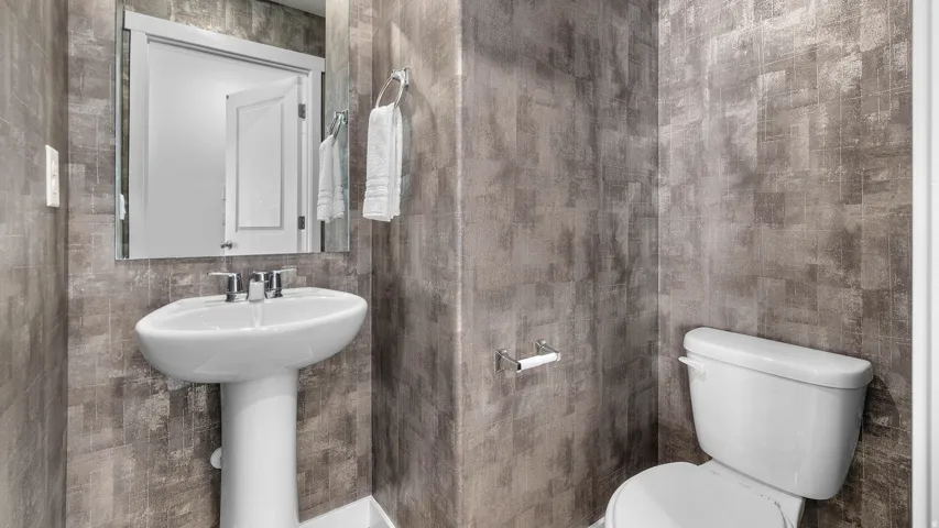 Pedestal sink with chrome fixtures, white toilet, and textured gray wall covering