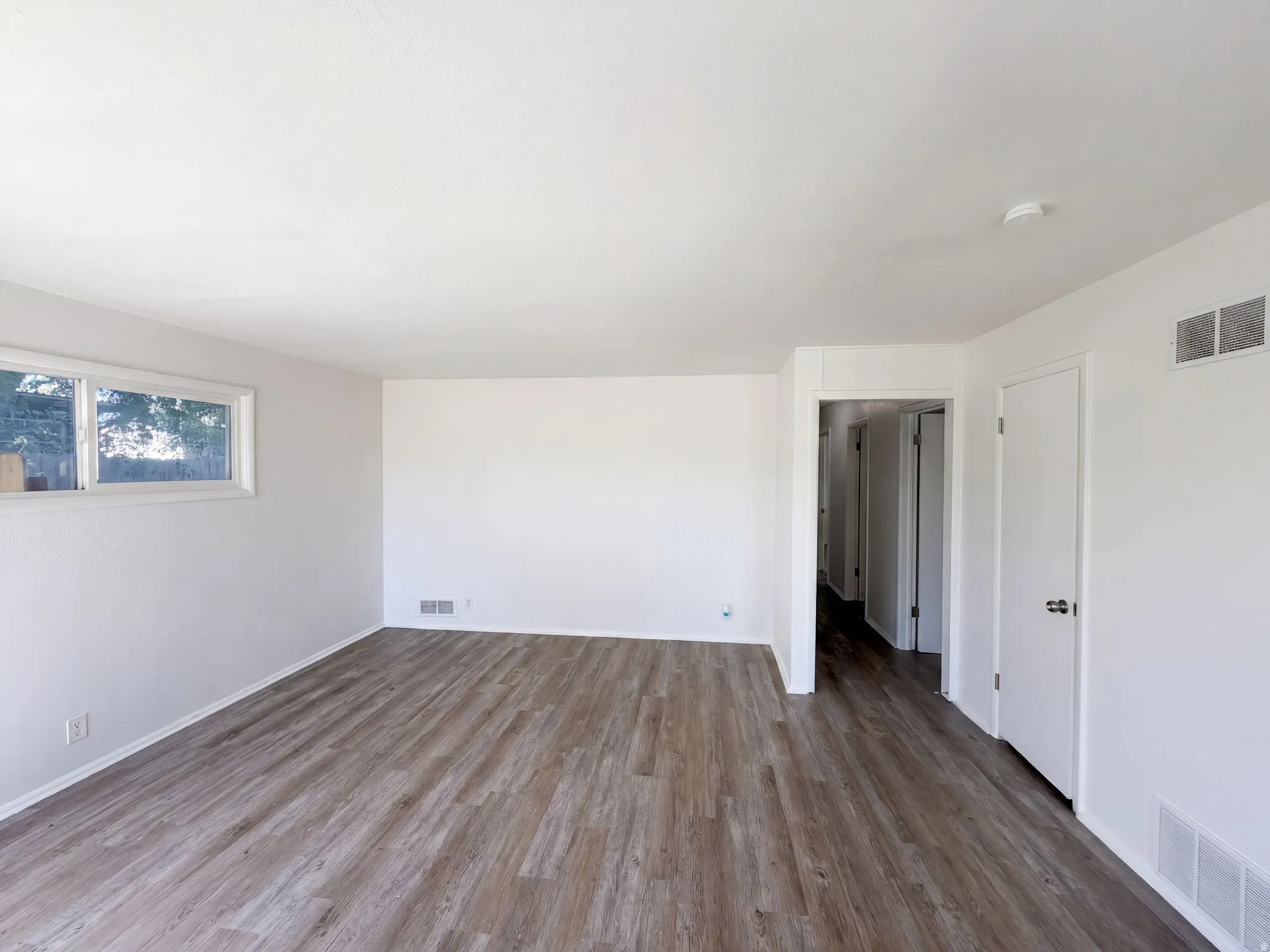 Expansive room featuring wood-finish flooring, white walls, and a window