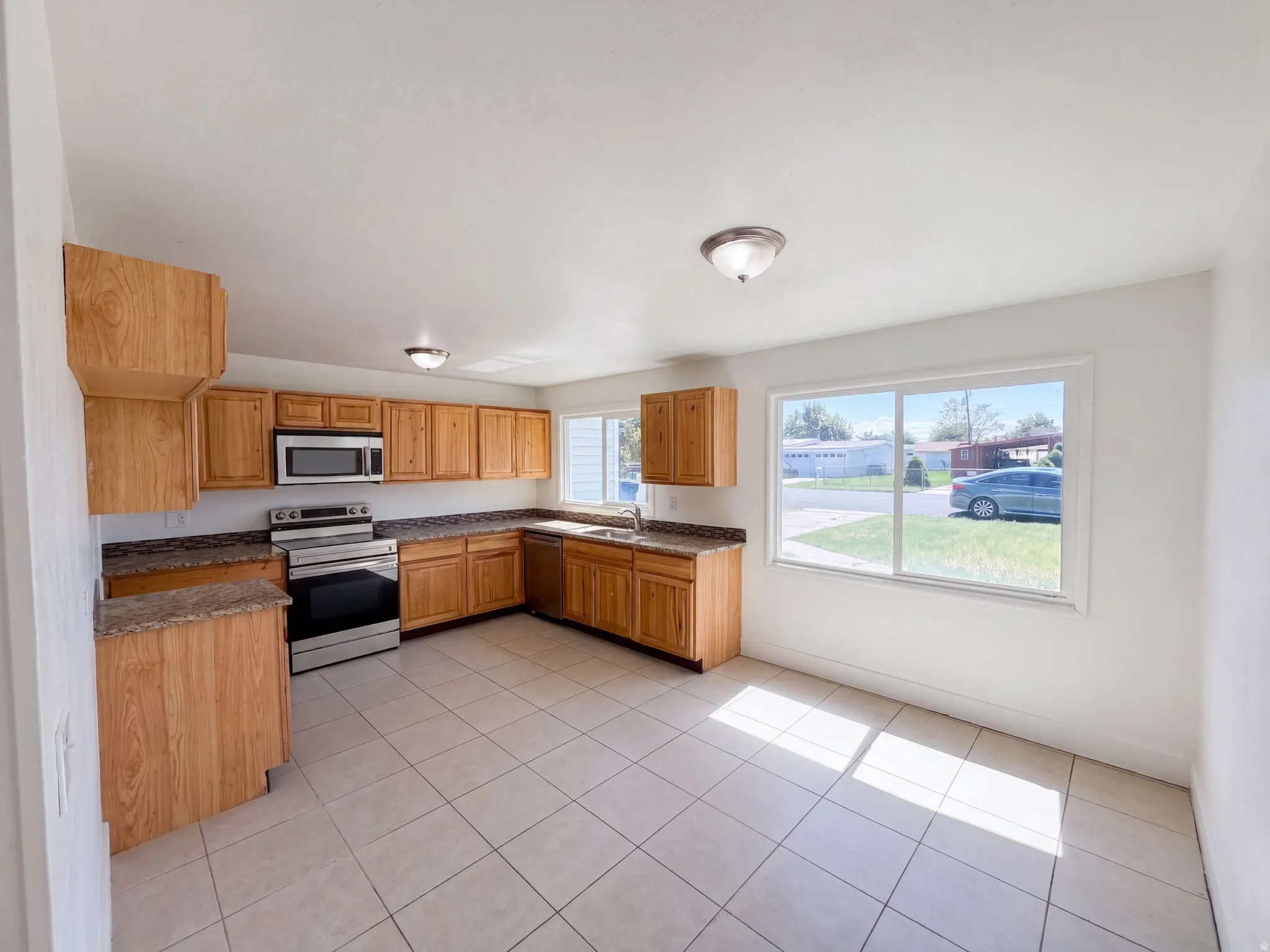 Kitchen featuring wood cabinetry, stone-finish countertops, stainless steel appliances, and tile flooring