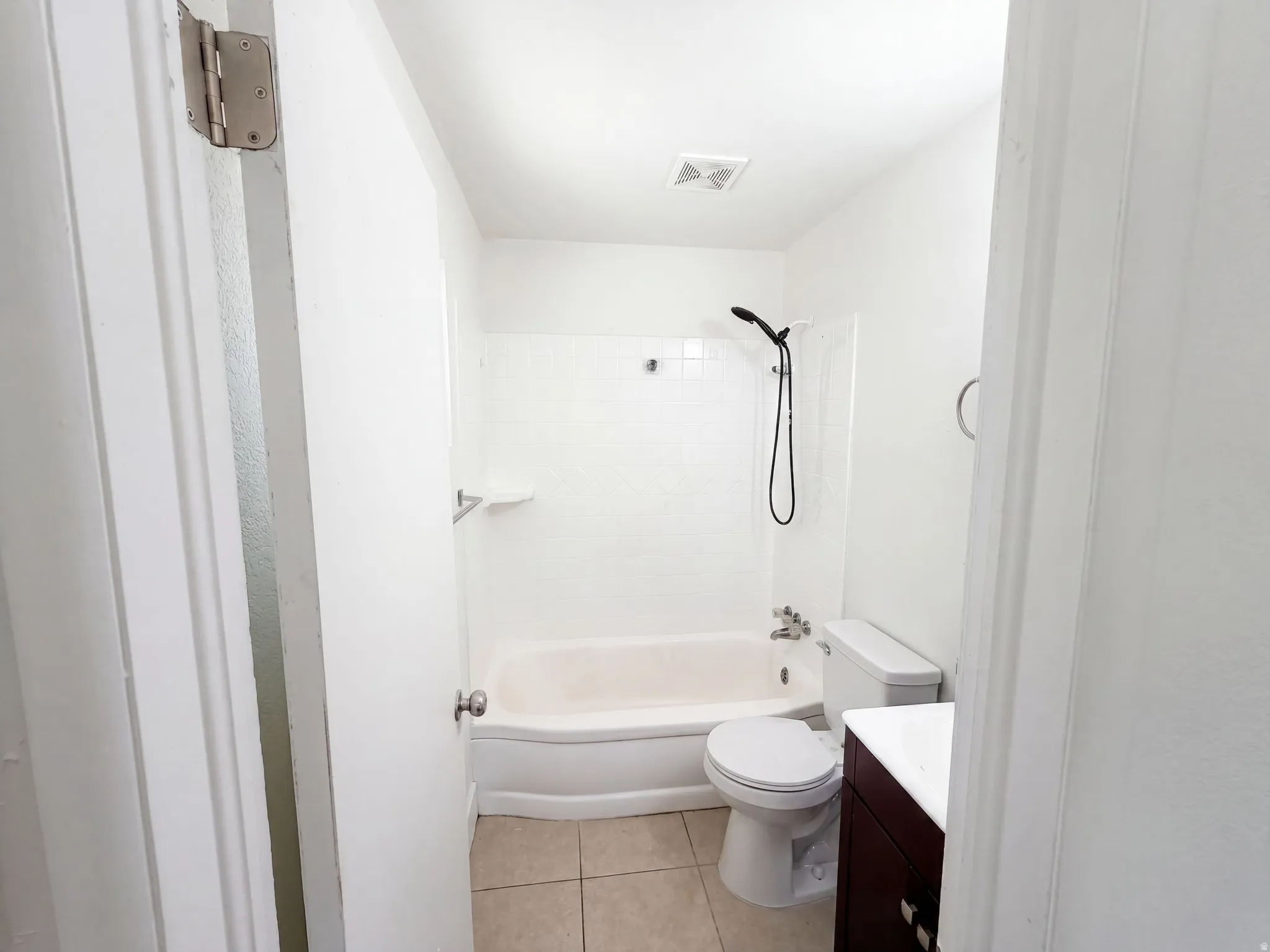 White tiled shower surround, recessed bathtub, and a dark wood-finish vanity with a white countertop