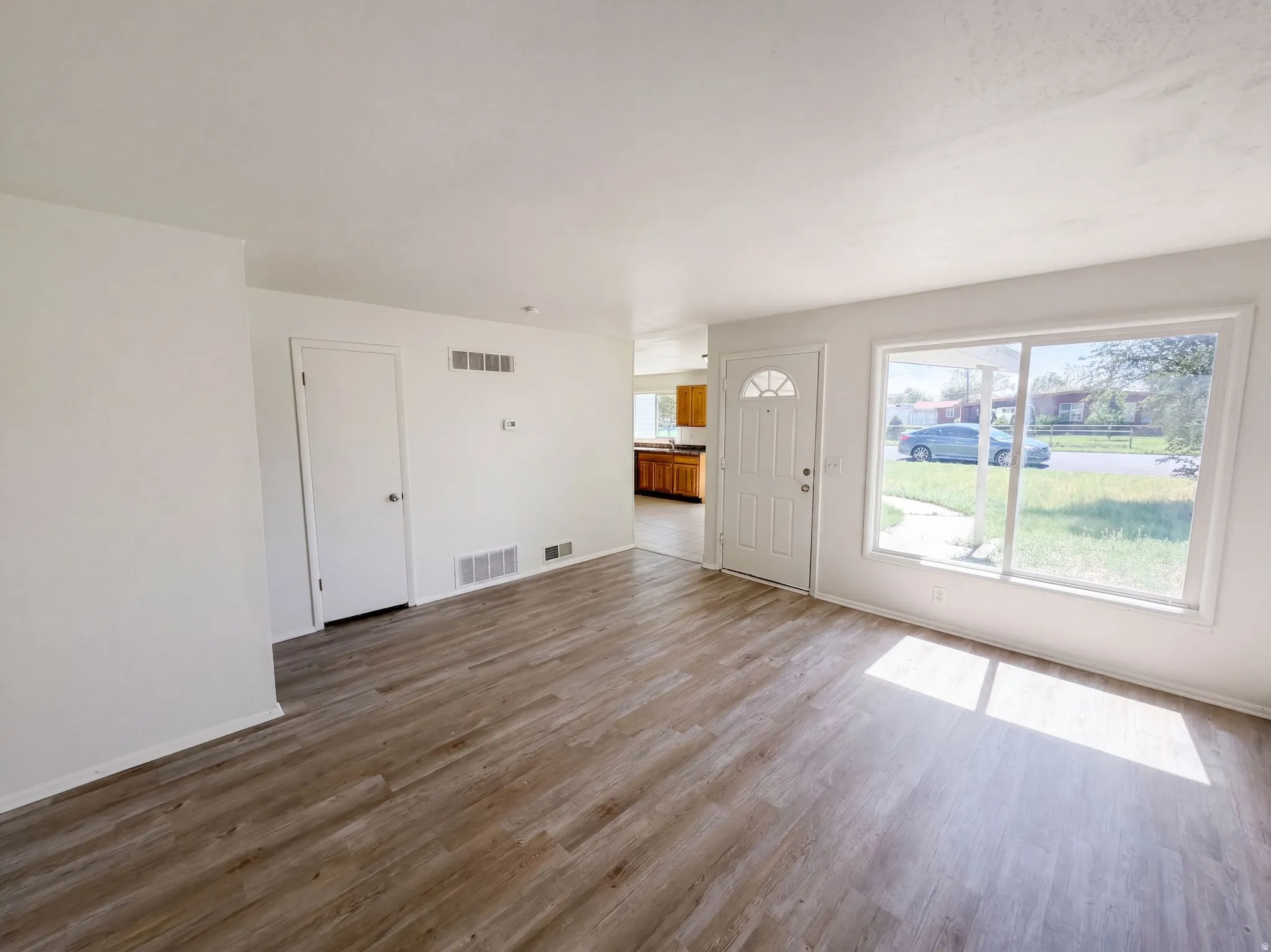 Spacious living area featuring wood-finish flooring, white walls, and a large picture window