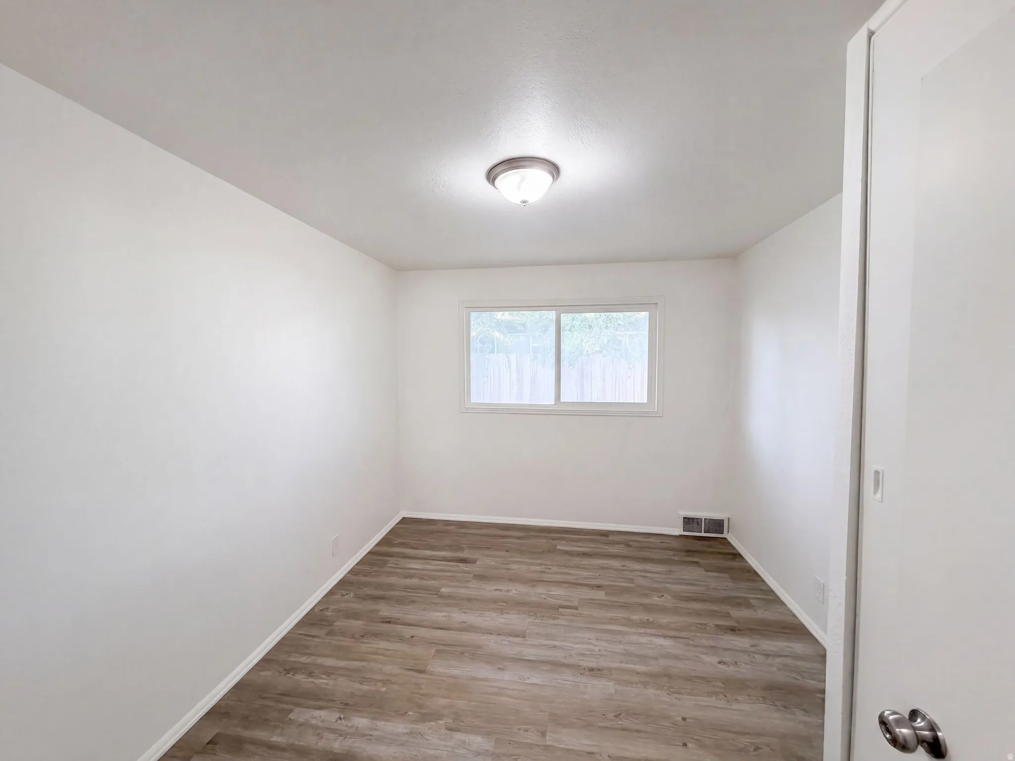 Bright secondary bedroom featuring wood-finish flooring, recessed ceiling lighting, and a large window allowing abundant natural light