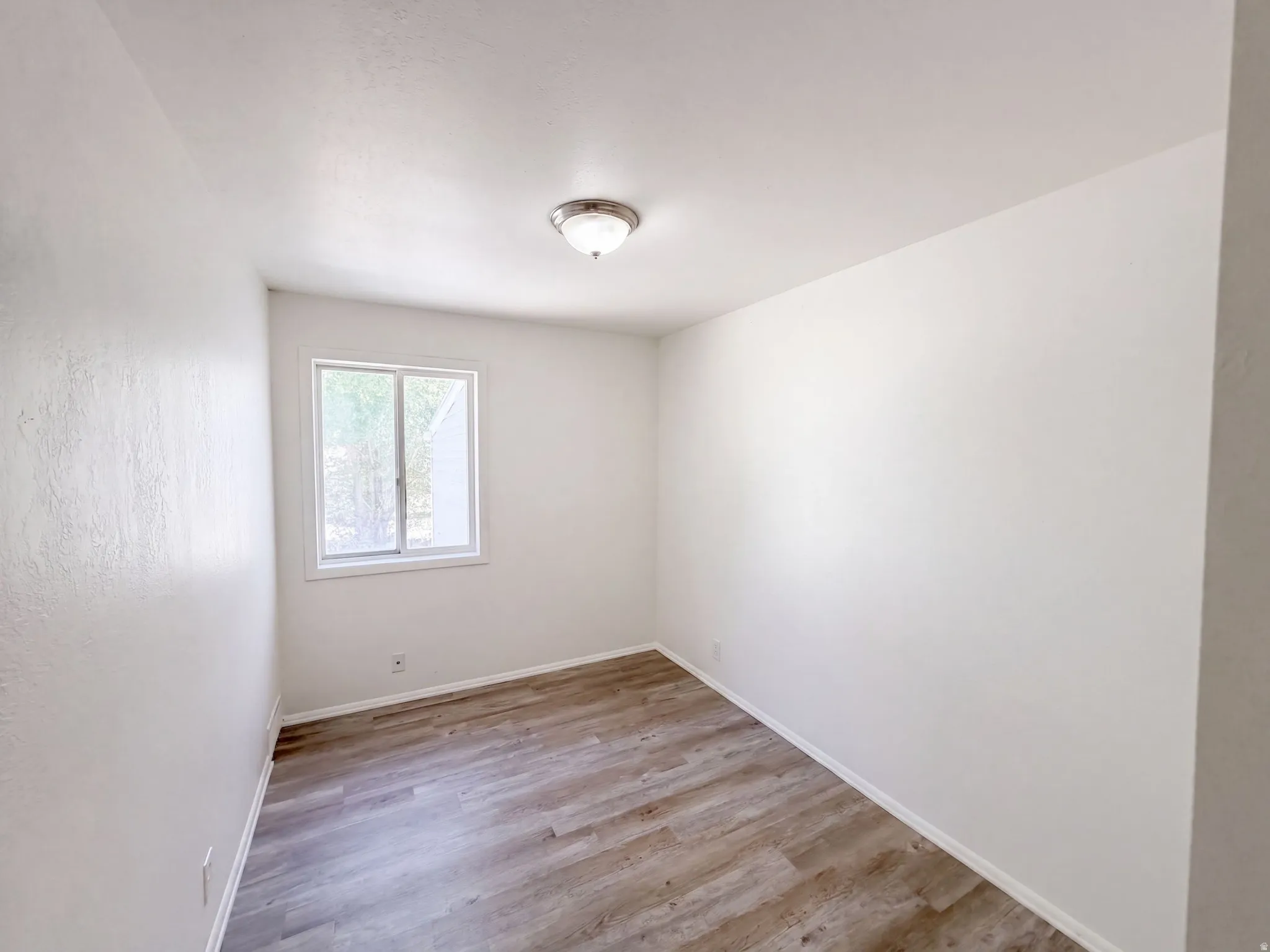 Bright and spacious bedroom featuring wood-finish flooring, neutral wall finishes, and a fixed ceiling light fixture