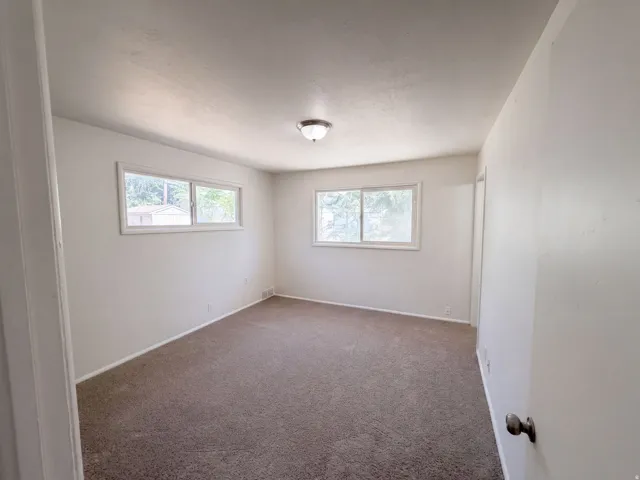 Bright secondary bedroom featuring carpet flooring, dual windows with natural light, and clean white walls with neutral finishes throughout