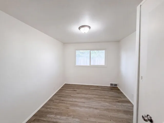 Bright secondary bedroom featuring wood-finish flooring, recessed ceiling lighting, and a large window allowing abundant natural light