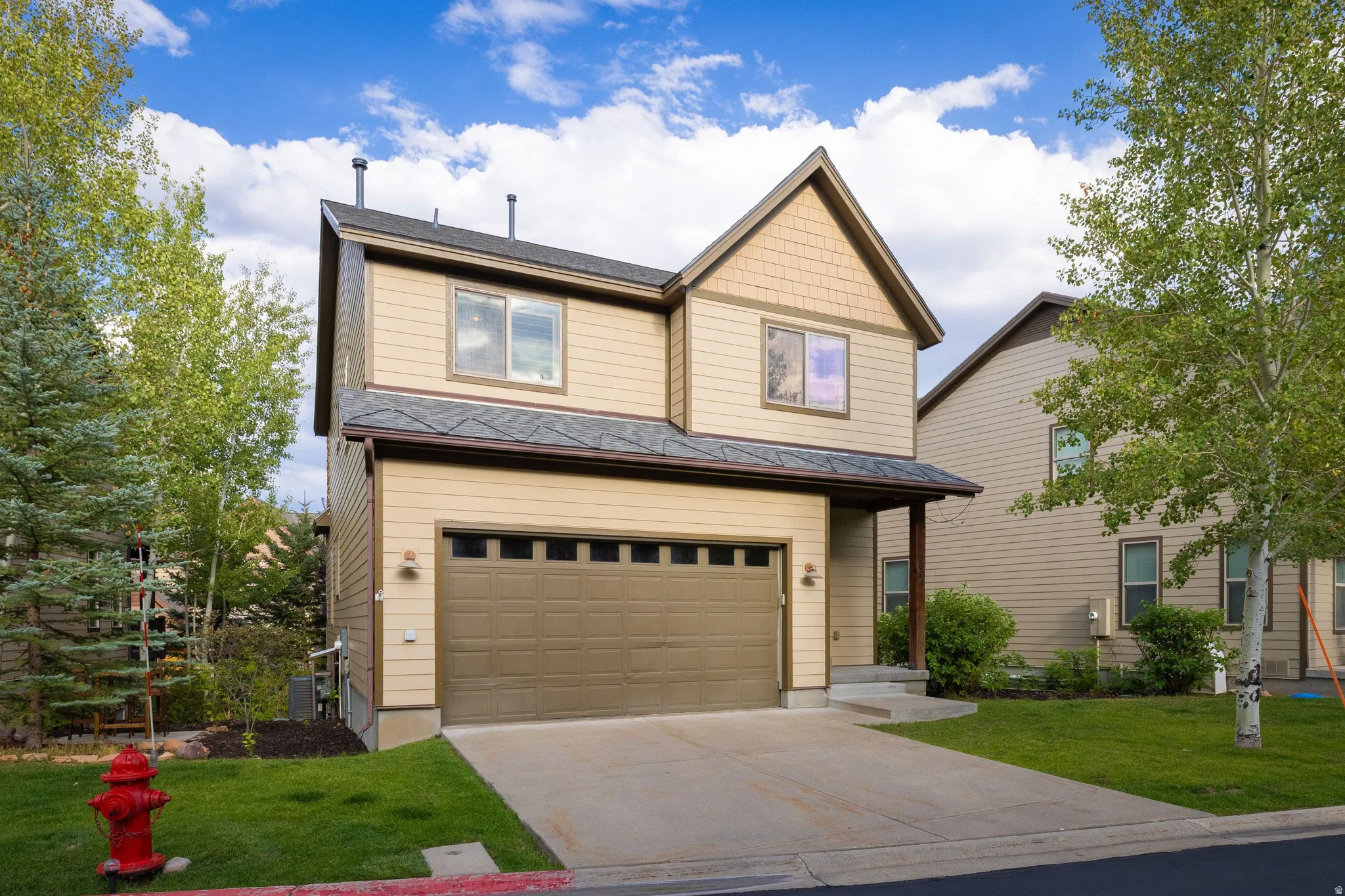 Two-story home featuring a tan and charcoal exterior with gabled roofline, dual-pane windows, and a two-car garage with horizontal panel doors