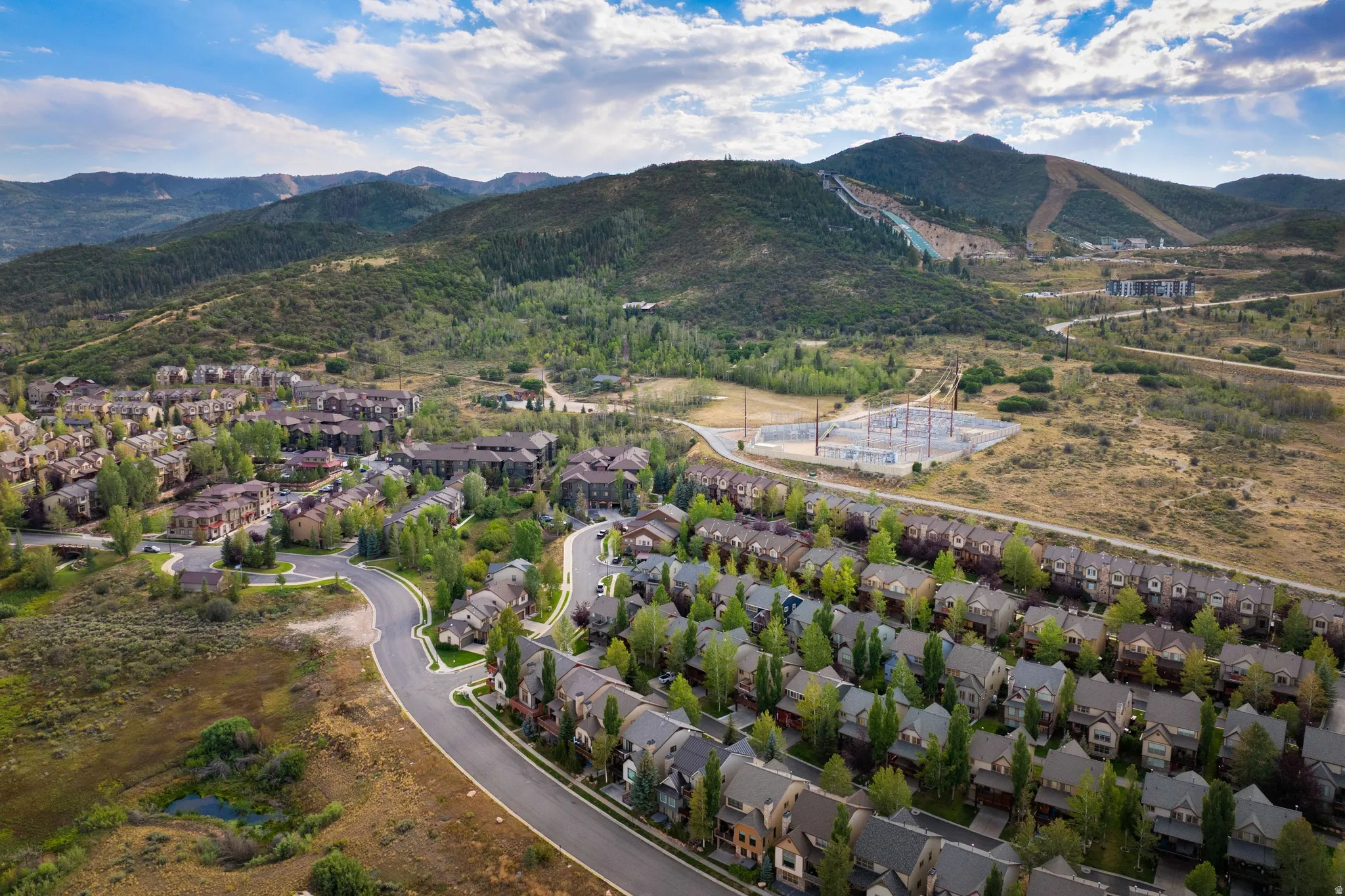 Masterfully planned residential community nestled in a verdant valley setting, featuring curved street design with mature landscaping, multi-unit architecture with consistent architectural styling, and expansive mountain backdrop