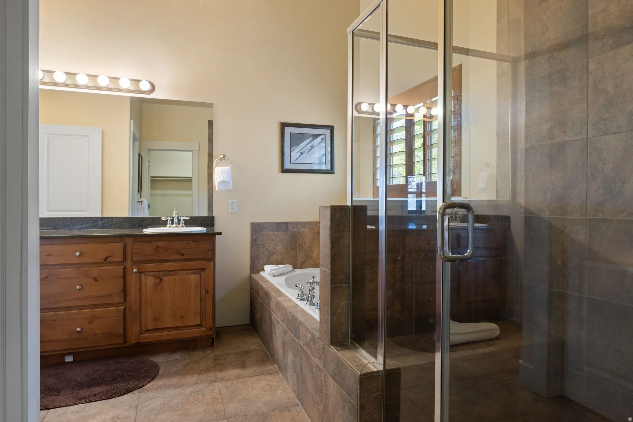 Spa-inspired primary bathroom featuring a wood-finish vanity with dual sinks, tile flooring, and a spacious walk-in shower enclosed in frameless glass with stone surround