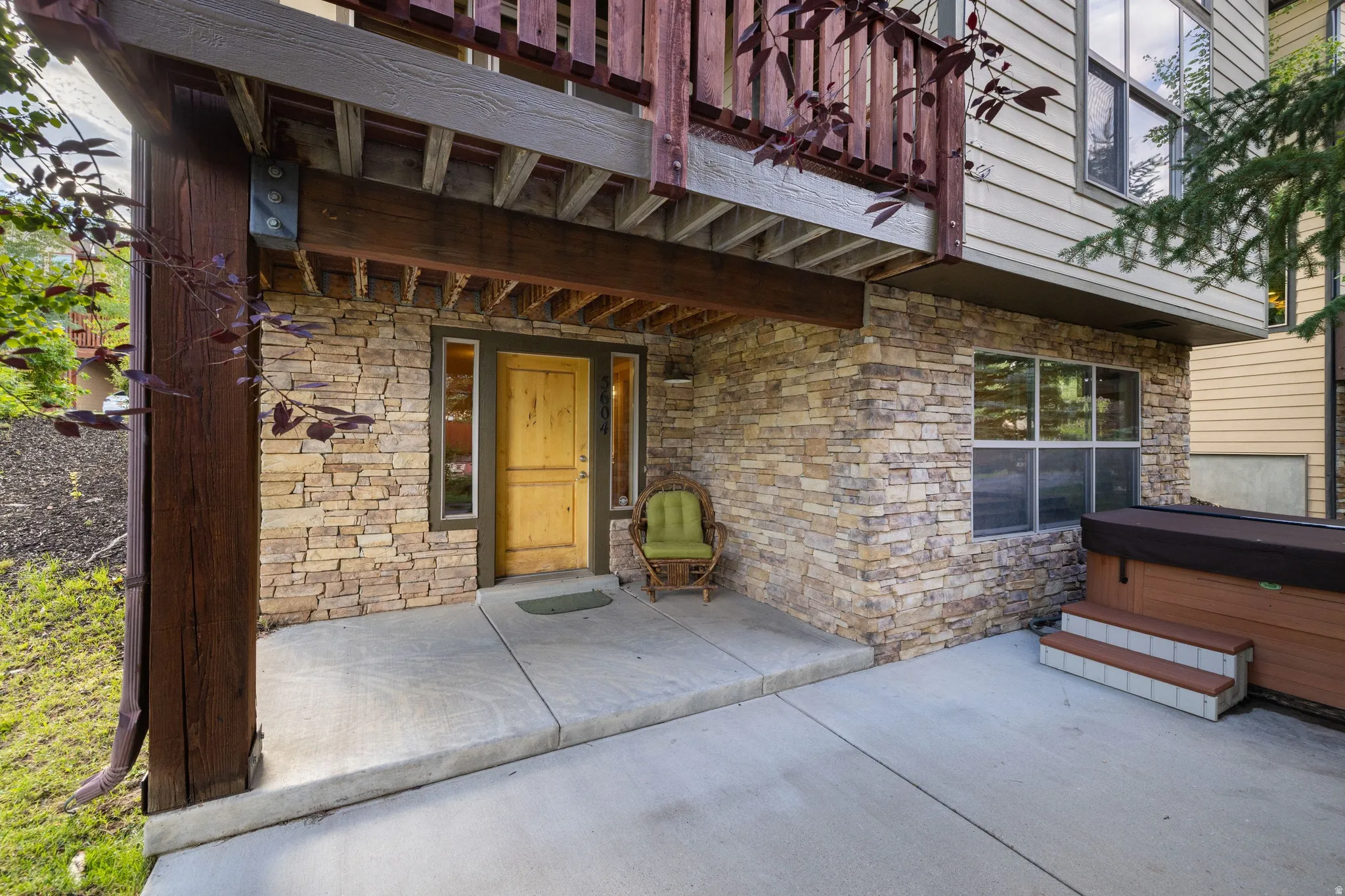 Covered entry patio featuring exposed brick veneer, concrete flooring, and a solid wood entry door with sidelights