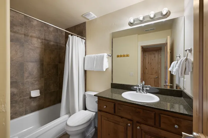Spa-inspired bathroom featuring a wood-finish vanity with ample storage, dark stone countertop, and round ceramic sink with chrome fixtures