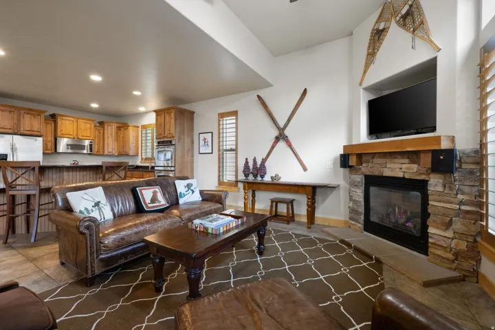 Open-concept living area featuring a wood-burning fireplace with stacked stone surround, recessed ceiling lighting, and wood cabinetry