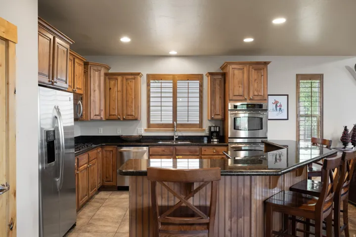 Chef's kitchen featuring custom wood cabinetry, stainless steel appliances, black granite countertops, and a large center island with seating