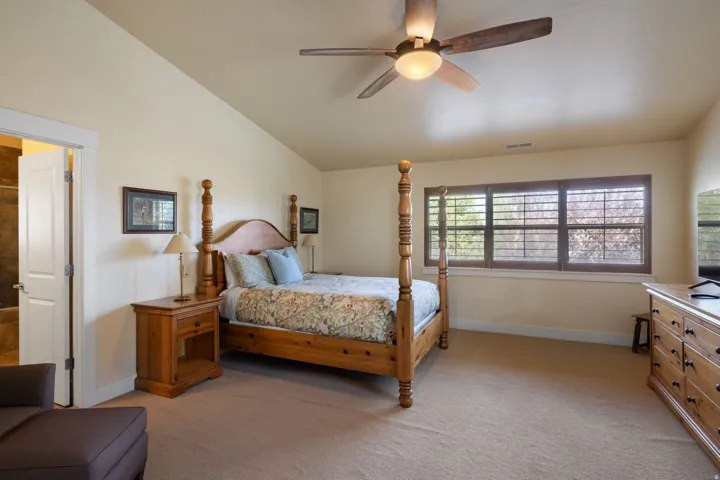 Spacious primary bedroom suite with soaring vaulted ceilings, ceiling fan with integrated lighting, and expansive windows with plantation shutters providing natural illumination