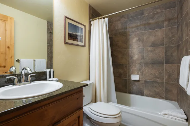 Spa-inspired bathroom featuring a ceramic pedestal sink with chrome faucet, slate-tiled shower enclosure with white curtain rod, white subway tile accents, and warm yellow walls