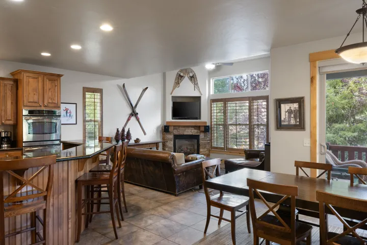Open-concept living area featuring a wood-finish bar with seating, tile flooring, recessed ceiling lighting, a fireplace with decorative mantel, built-in cabinetry, and large windows with interior shutters overlooking outdoor grounds