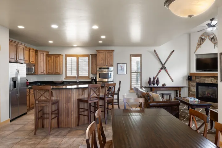 Open-concept kitchen and dining area featuring wood cabinetry, stainless steel appliances, a center island with seating, wood-finish flooring, and a fireplace with stone surround in the adjacent living space