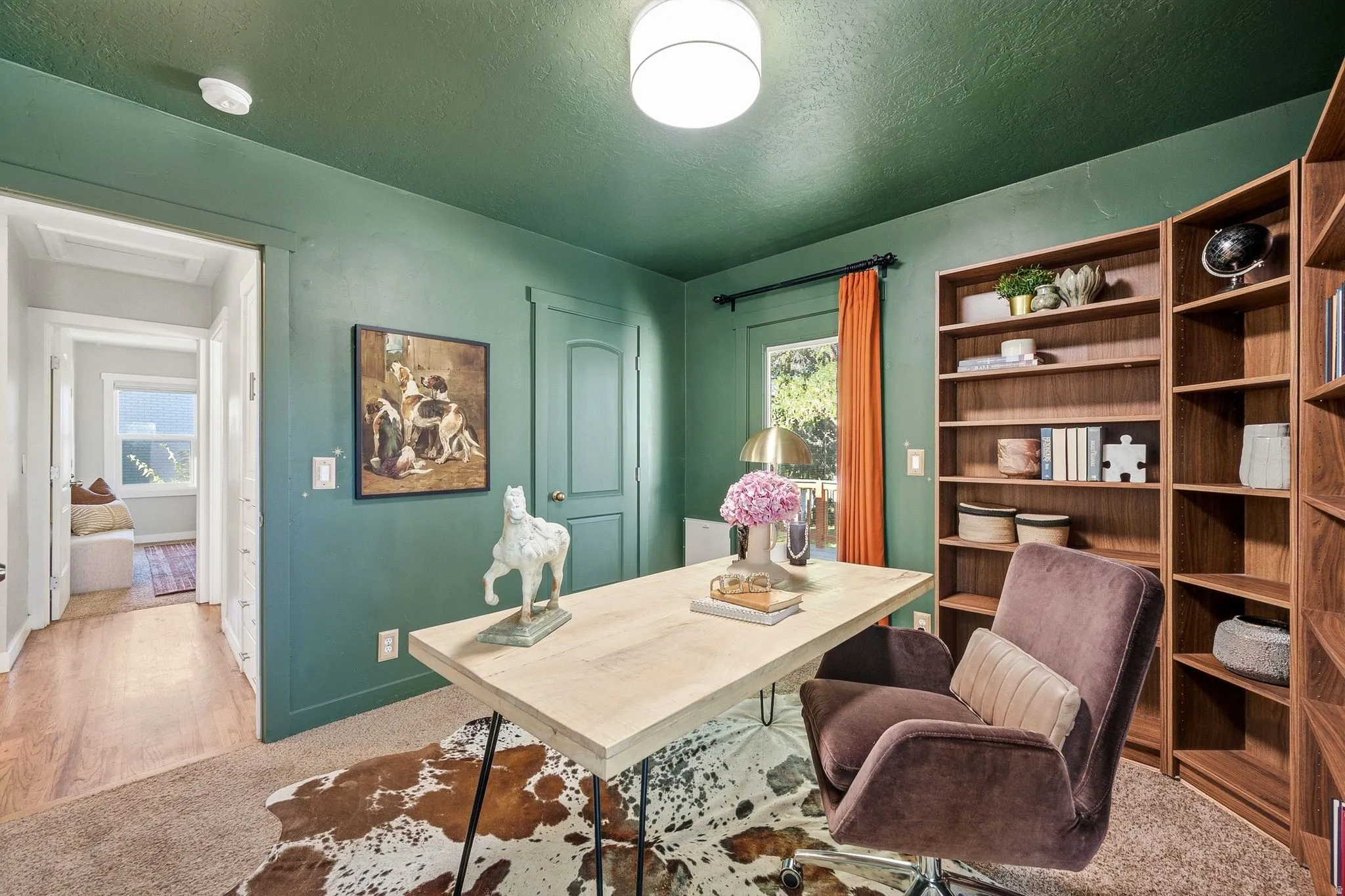 Sophisticated home office featuring soft sage-green walls, recessed ceiling lighting, and expansive wood-finish built-in shelving with open storage