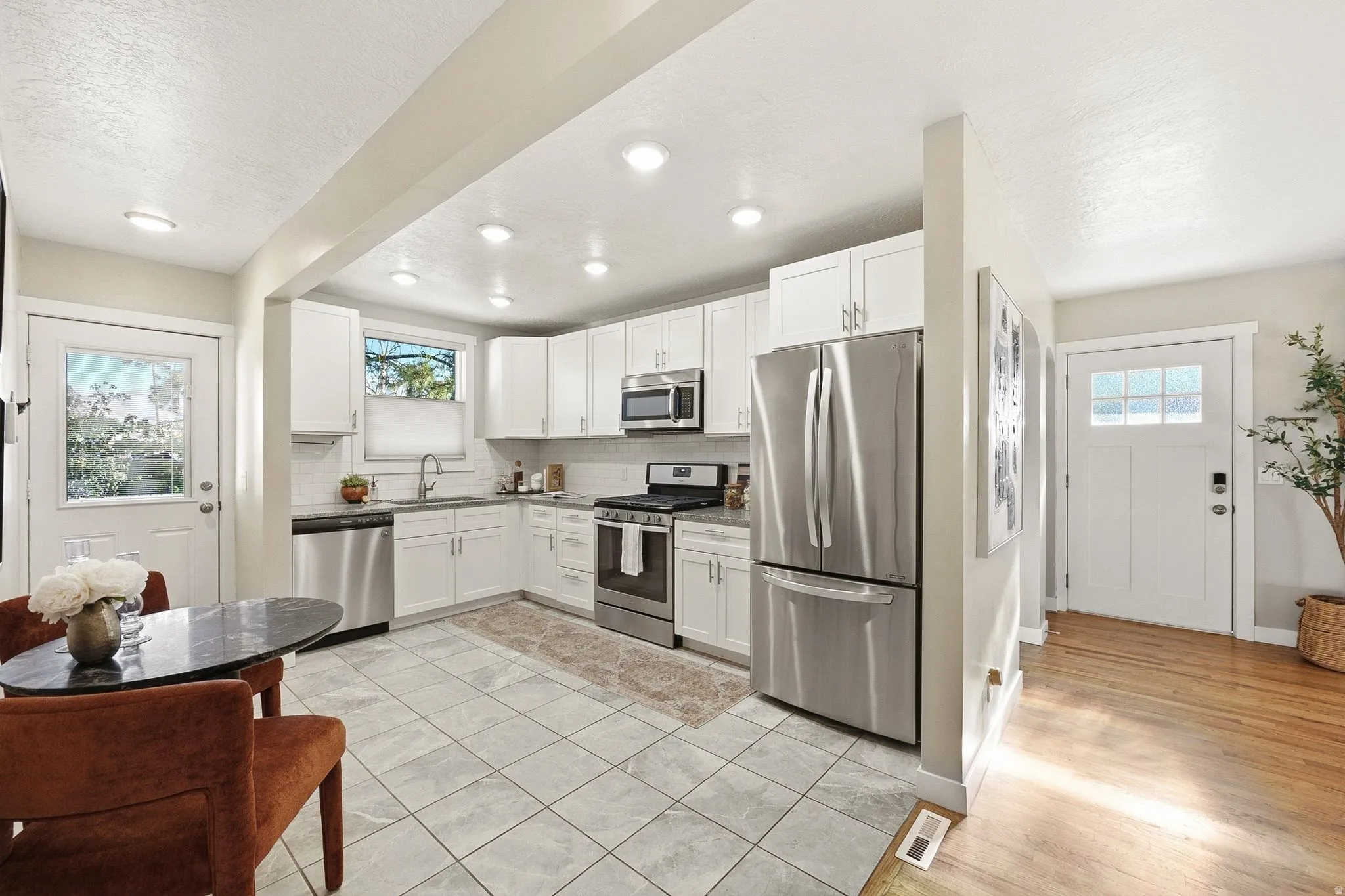 Modern kitchen featuring white cabinetry, stainless steel appliances including a French-door refrigerator and gas range, tile flooring, recessed lighting, and granite-style countertops