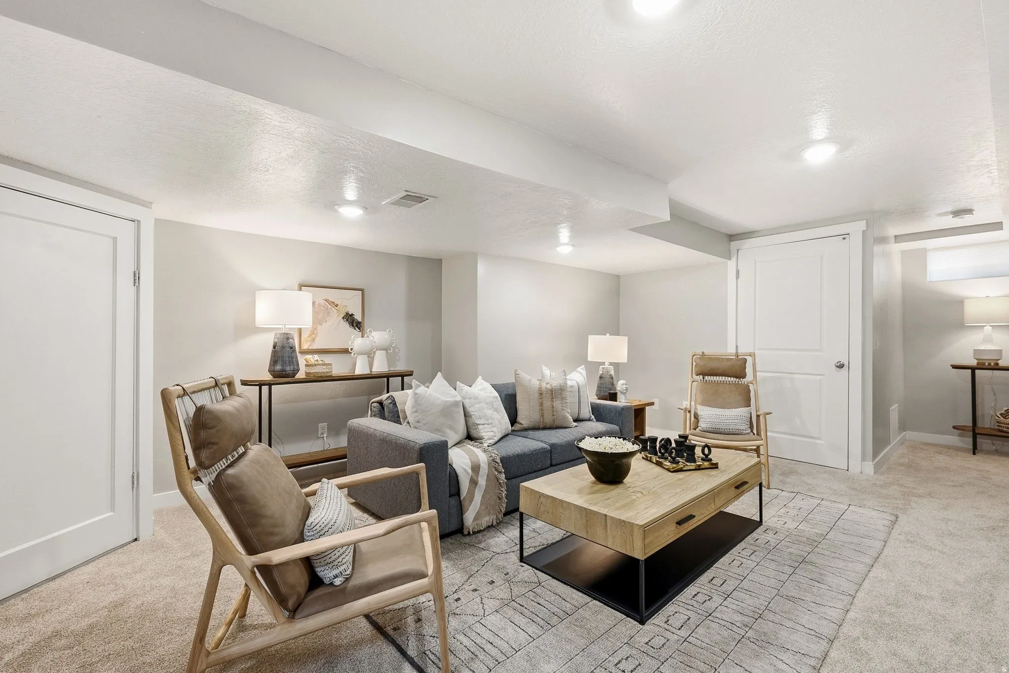 Sophisticated basement recreation area featuring recessed ceiling lighting, neutral-toned carpet flooring, and a wood-finish console table with metal base