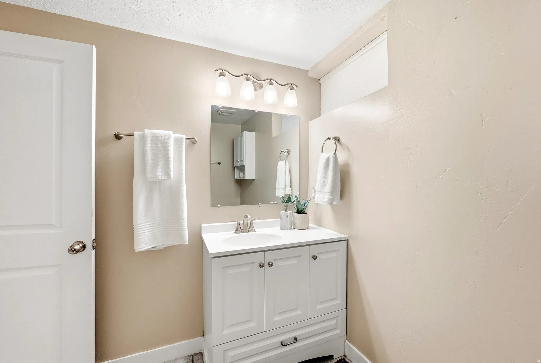 Bright bathroom featuring a white cabinetry vanity with dual storage, ceramic sink, polished chrome fixtures, and mirrored medicine cabinet