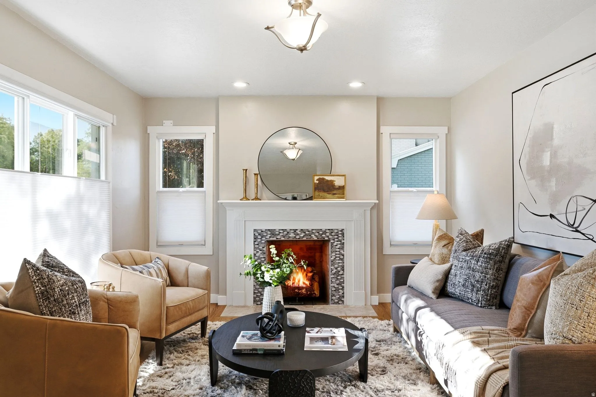 Elegant living room featuring a wood-burning fireplace with decorative surround, recessed ceiling lighting, large windows with natural light, neutral wall finishes, and hardwood flooring throughout