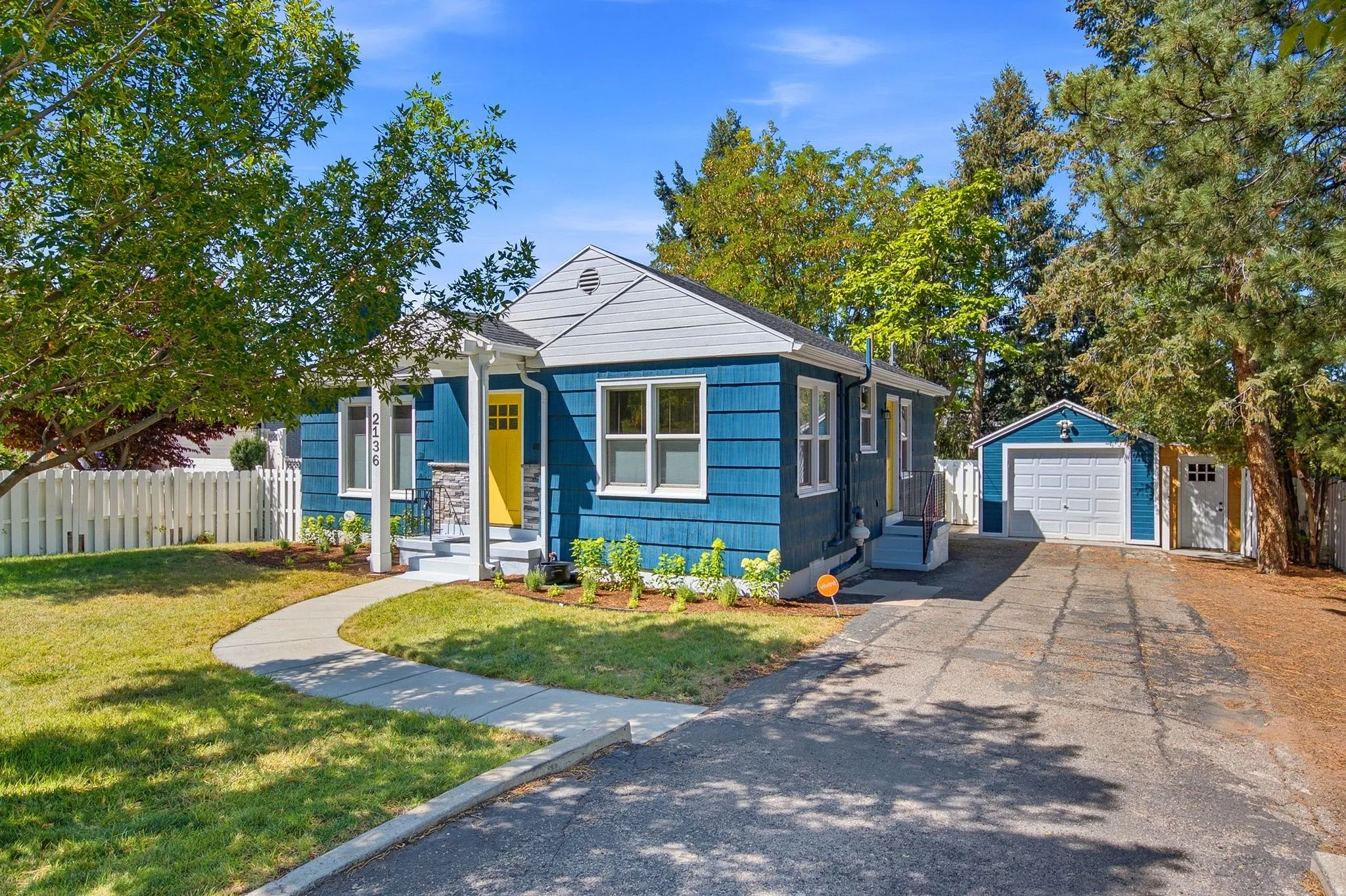 Charming blue cottage with yellow accent door and board-and-batten siding, featuring a gabled roofline and multiple windows allowing natural light