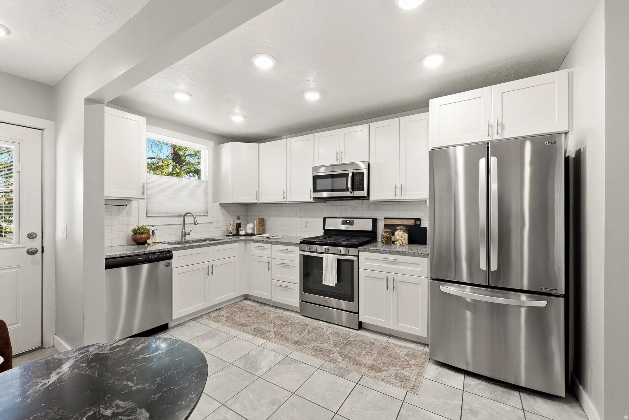 Modern kitchen featuring white cabinetry, stainless steel appliances including a French-door refrigerator and convection range, black granite countertops, tile flooring, recessed ceiling lighting, and a functional L-shaped layout with ample storage and wo