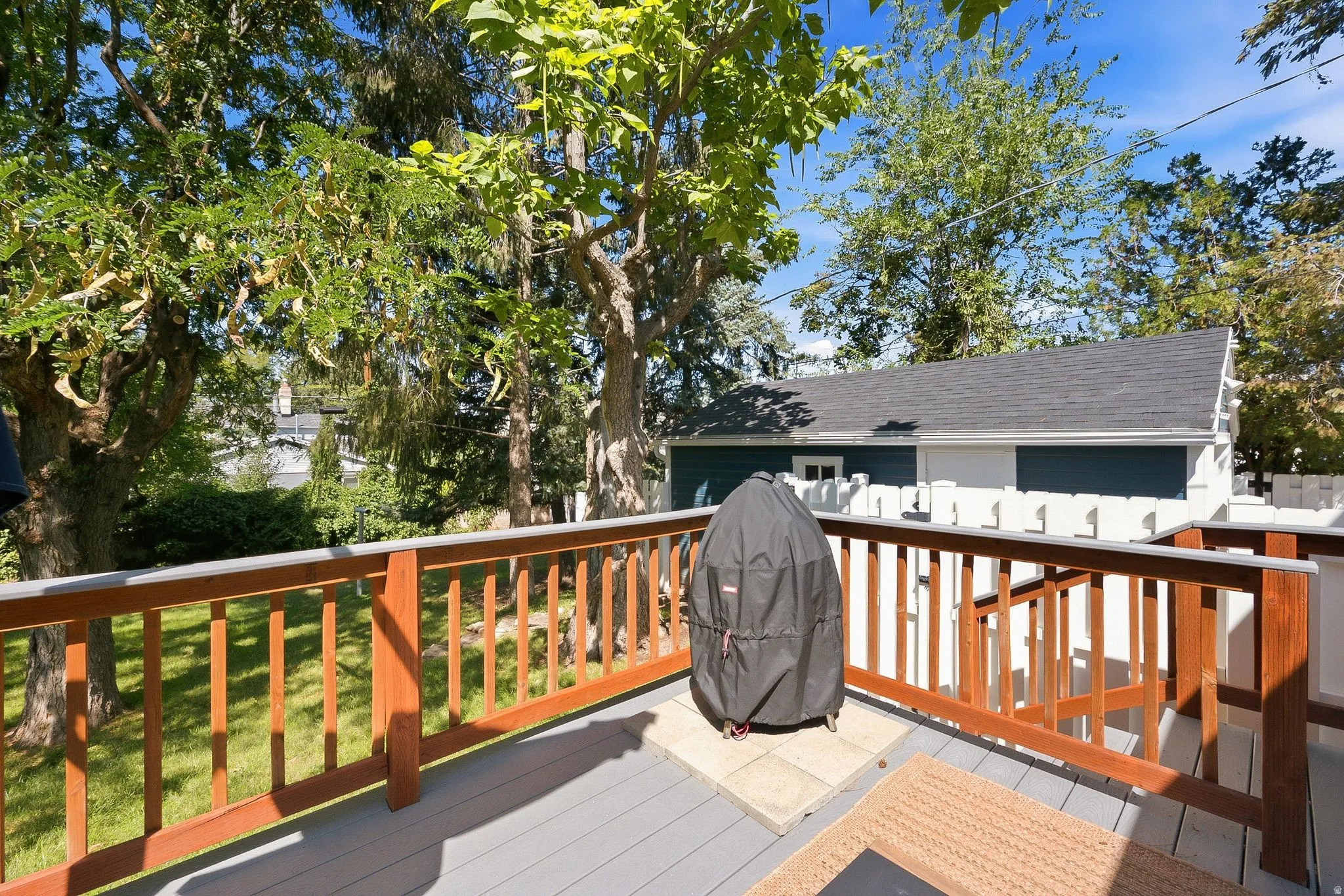 Expansive composite deck featuring warm wood-finish railings with decorative balusters, composite decking surface, and mature tree canopy overhead