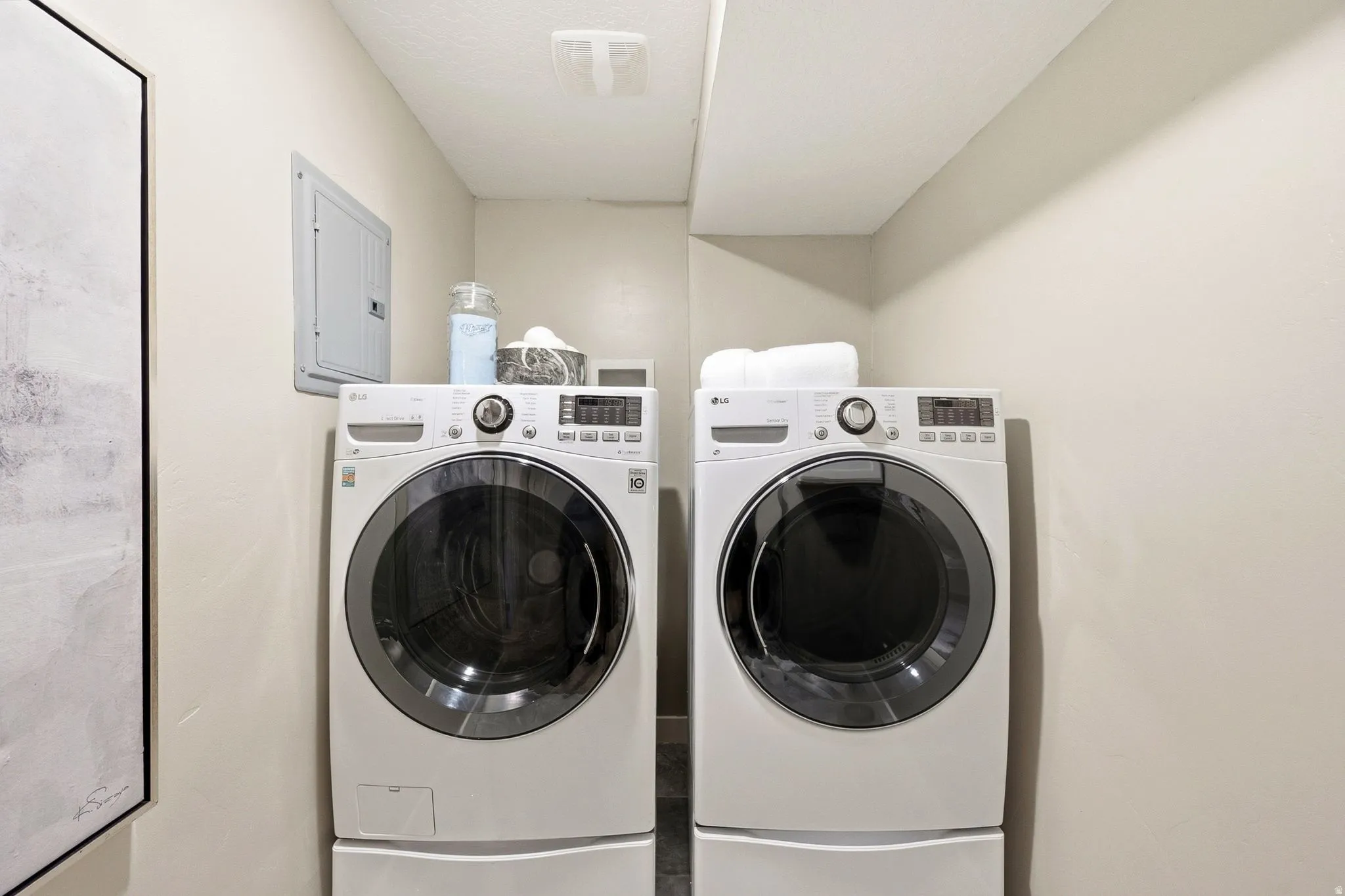 Dedicated laundry room featuring side-by-side front-load washers and dryers with digital controls, ample countertop storage above, and neutral wall finishes throughout