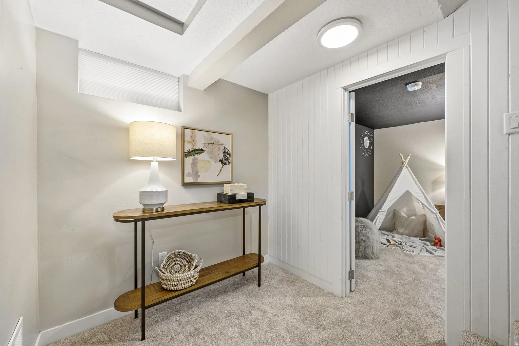 Recessed ceiling with exposed beam, egress window, carpet flooring, and a flush-mount ceiling light