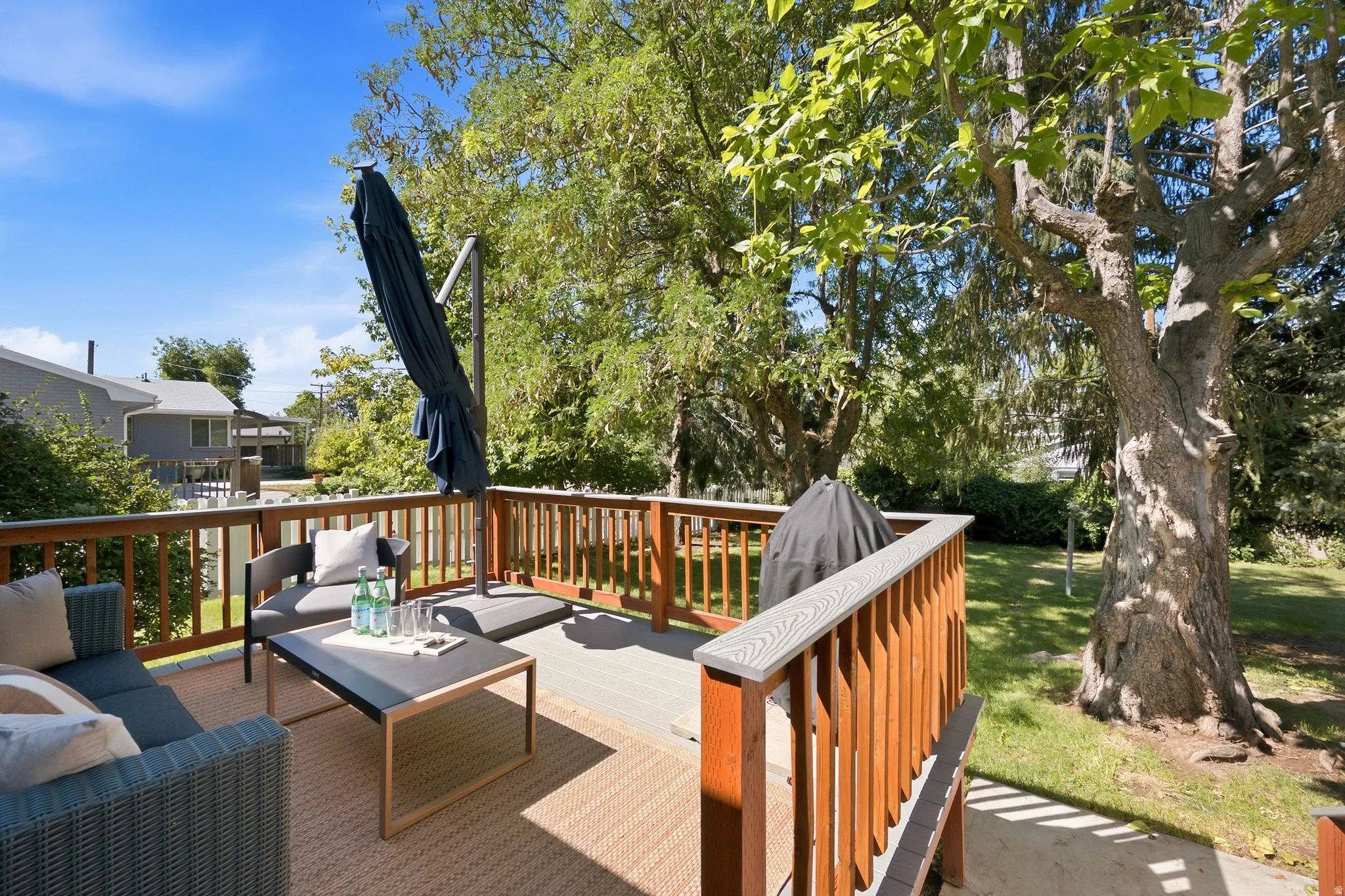 Expansive composite deck with wood-finish railings and integrated shade umbrella, overlooking manicured lawn and mature specimen trees