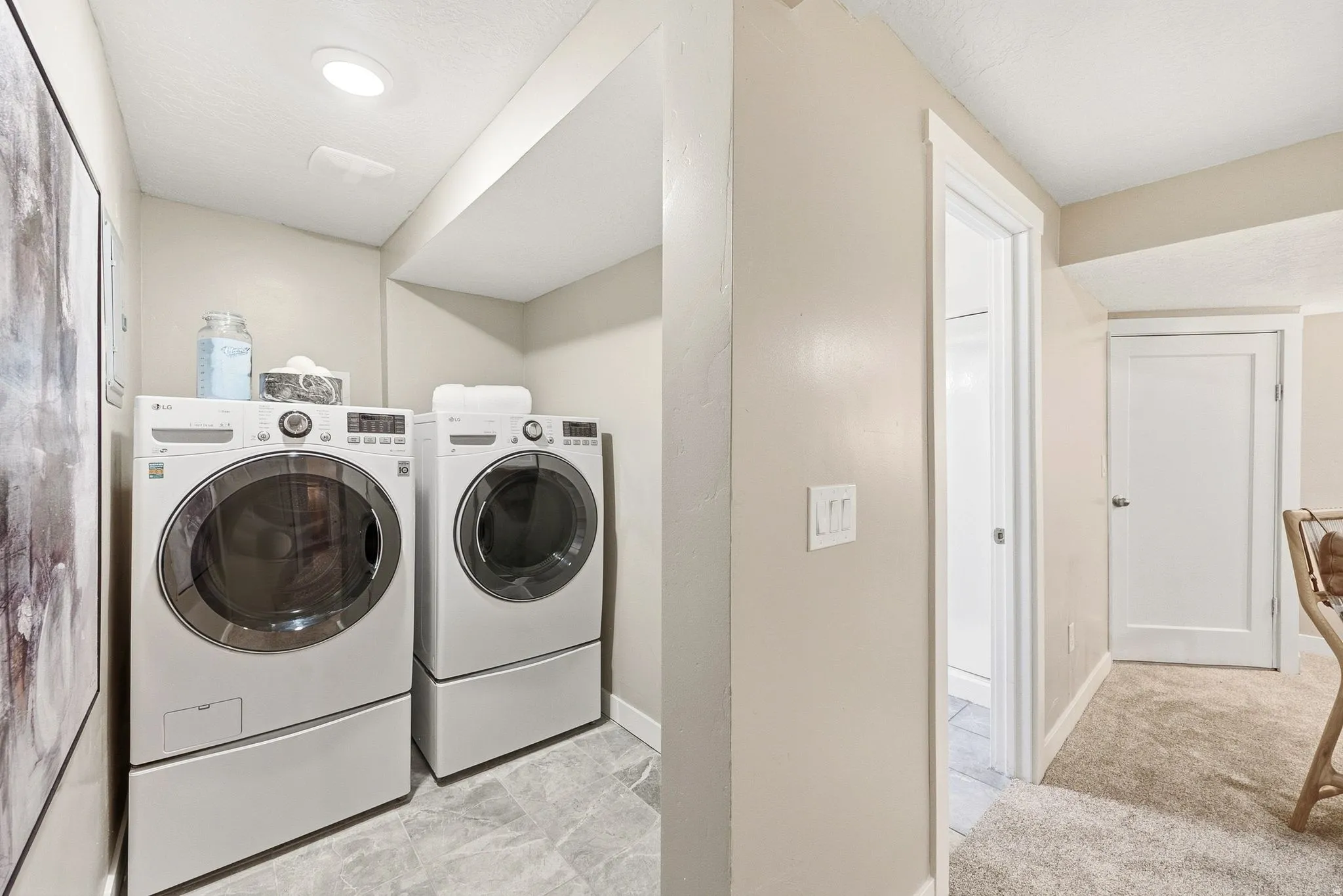 Dedicated laundry room featuring side-by-side front-load washers and dryers with pedestals, neutral tile flooring, recessed lighting, and direct access to adjacent spaces