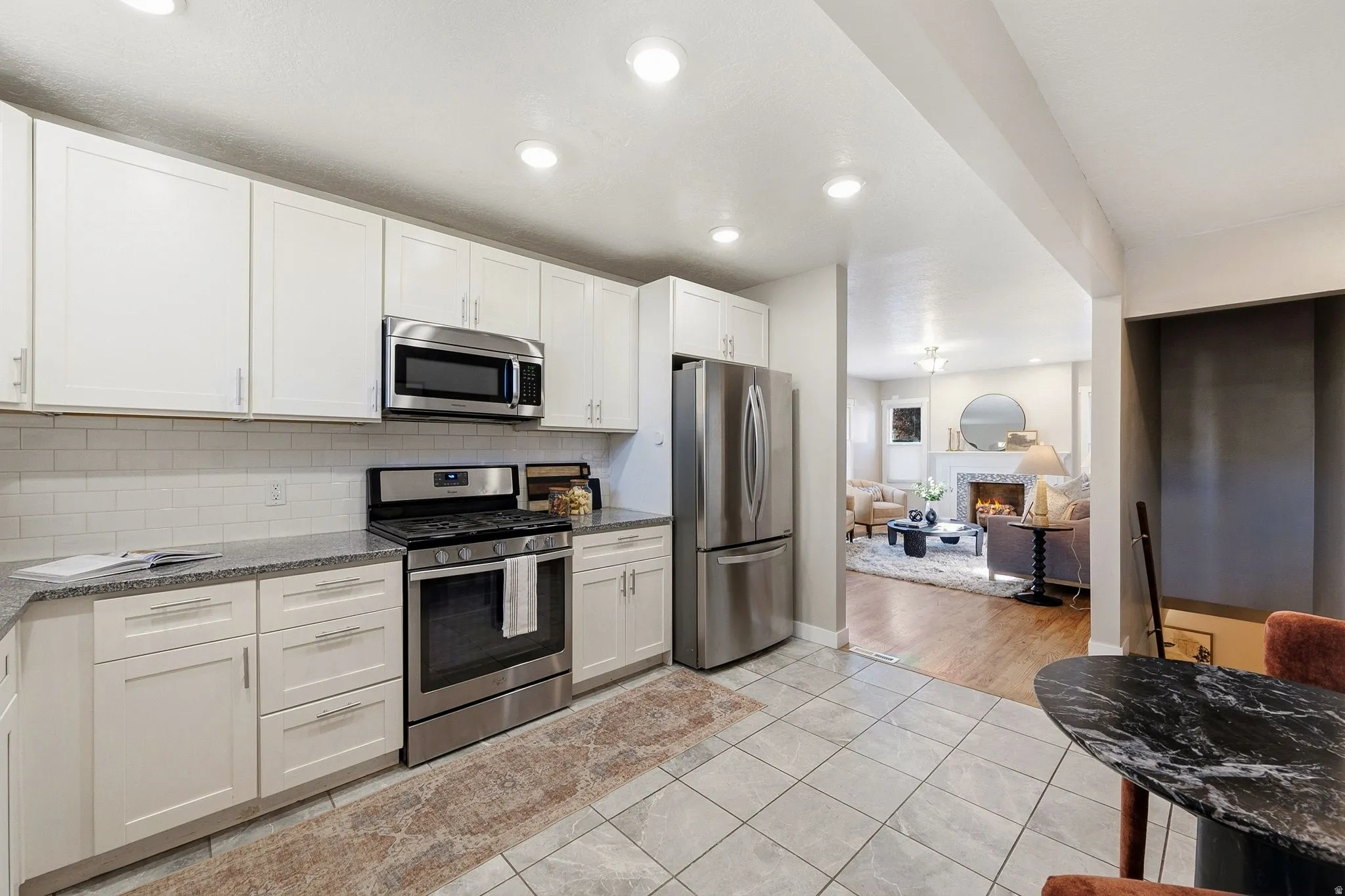 Modern kitchen featuring white cabinetry, stainless steel appliances including a gas range and over-the-range microwave, a French-door refrigerator, tile flooring, and a black granite-finish island with seating