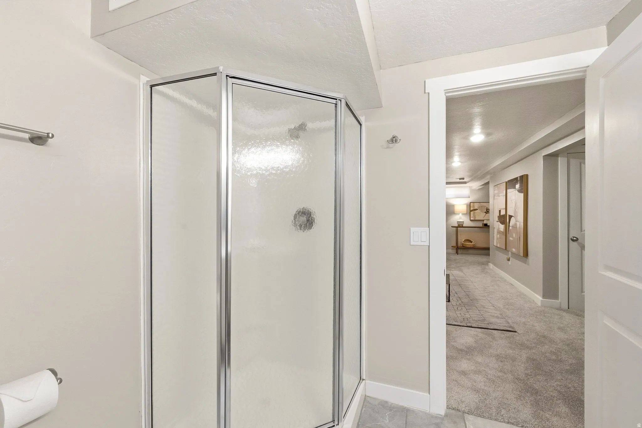Modern bathroom featuring a frameless glass corner shower enclosure with chrome hardware, ceramic tile flooring, white painted walls, and direct access to the hallway beyond