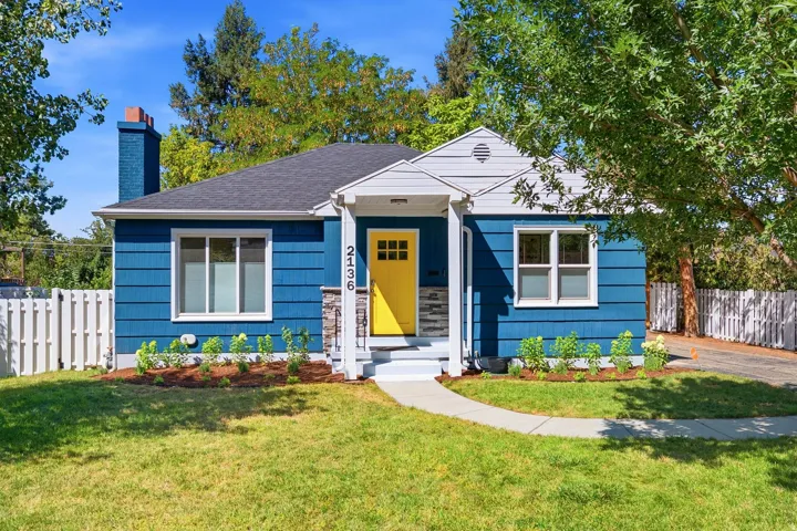 Charming blue cottage featuring a bright yellow entry door, white trim detailing, and a gabled roofline